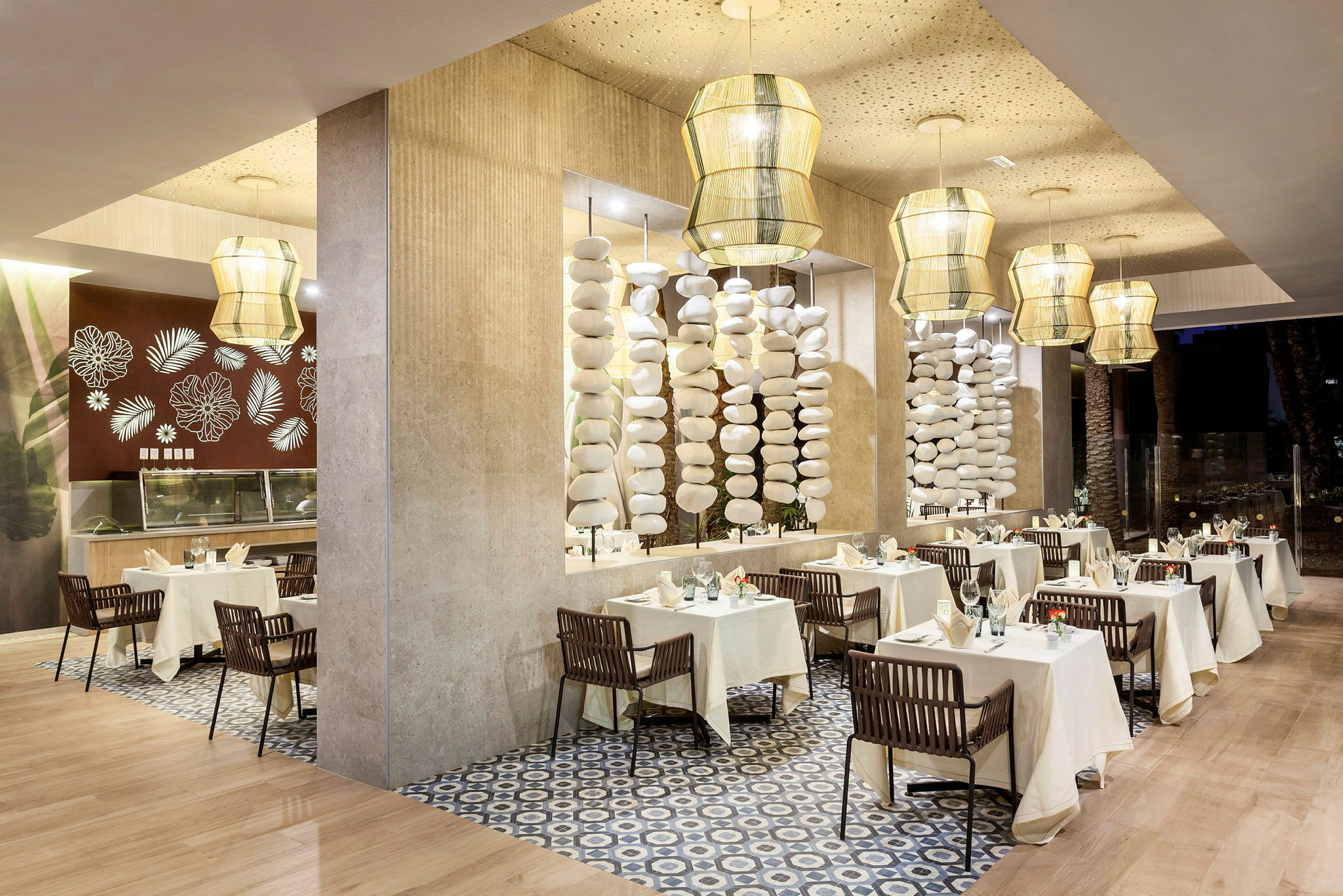 En elegant restaurantinteriør med bord dekket med hvite duker og stilfullt dekorert med porselen og glass. Lyse hengende lamper og dekorative søyler kompletterer designen. (AI-generert tekst)