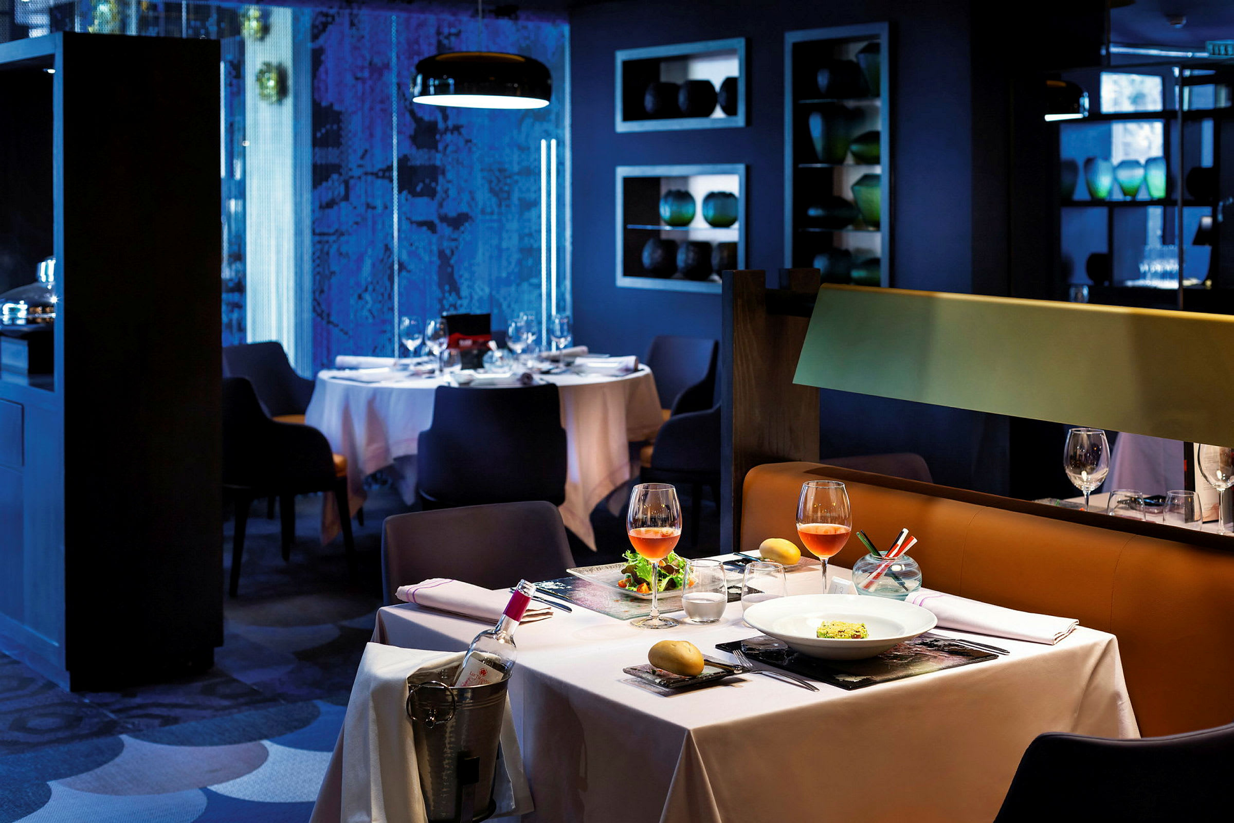 Et elegant restaurantbord med hvit duk, to vinglass og en anrettet rett. En vinflaske står avkjølt ved siden. (AI-generert tekst)