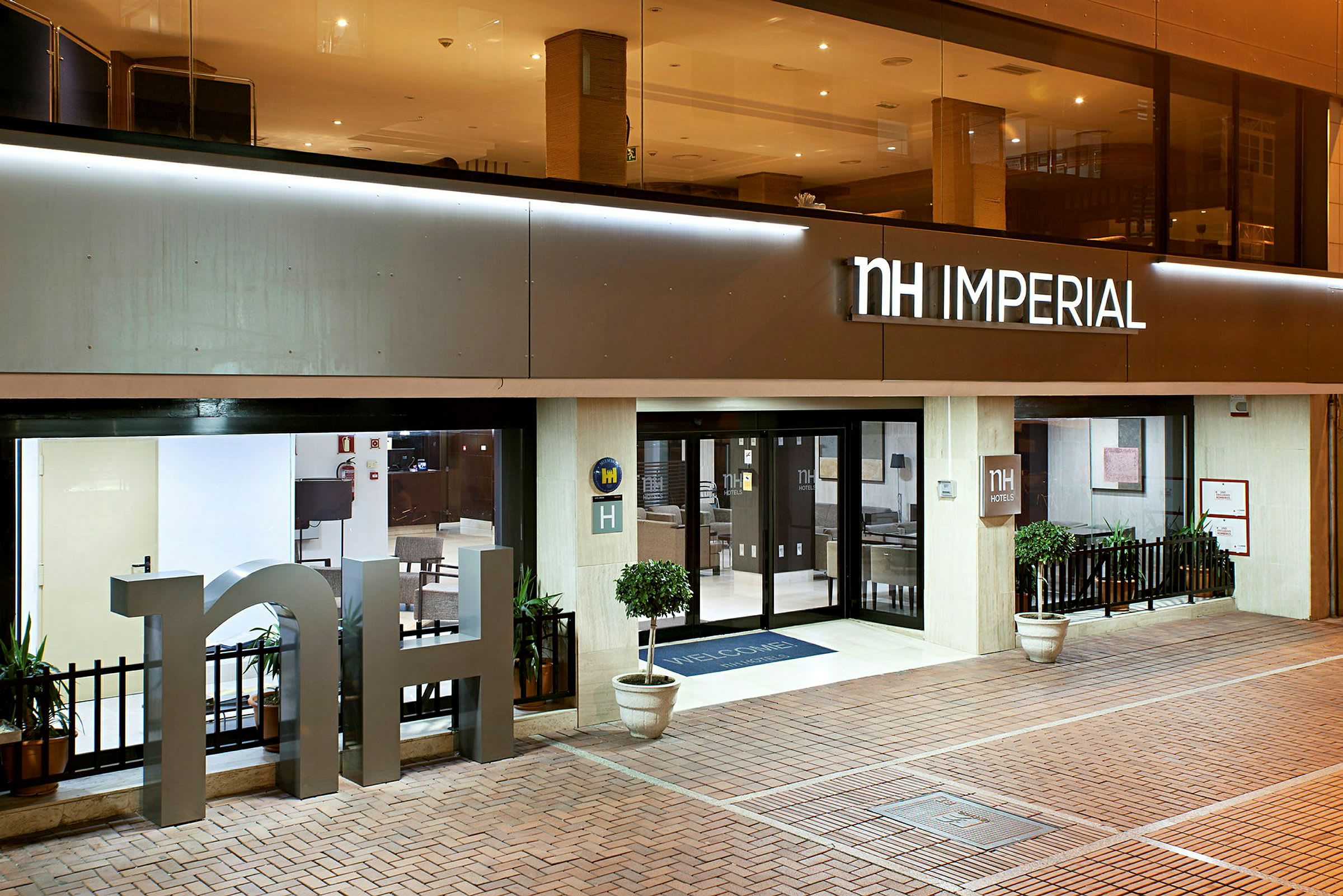 Inngangen til NH Imperial-hotellet med store glassdører og dekorasjoner. (AI-generert tekst)
