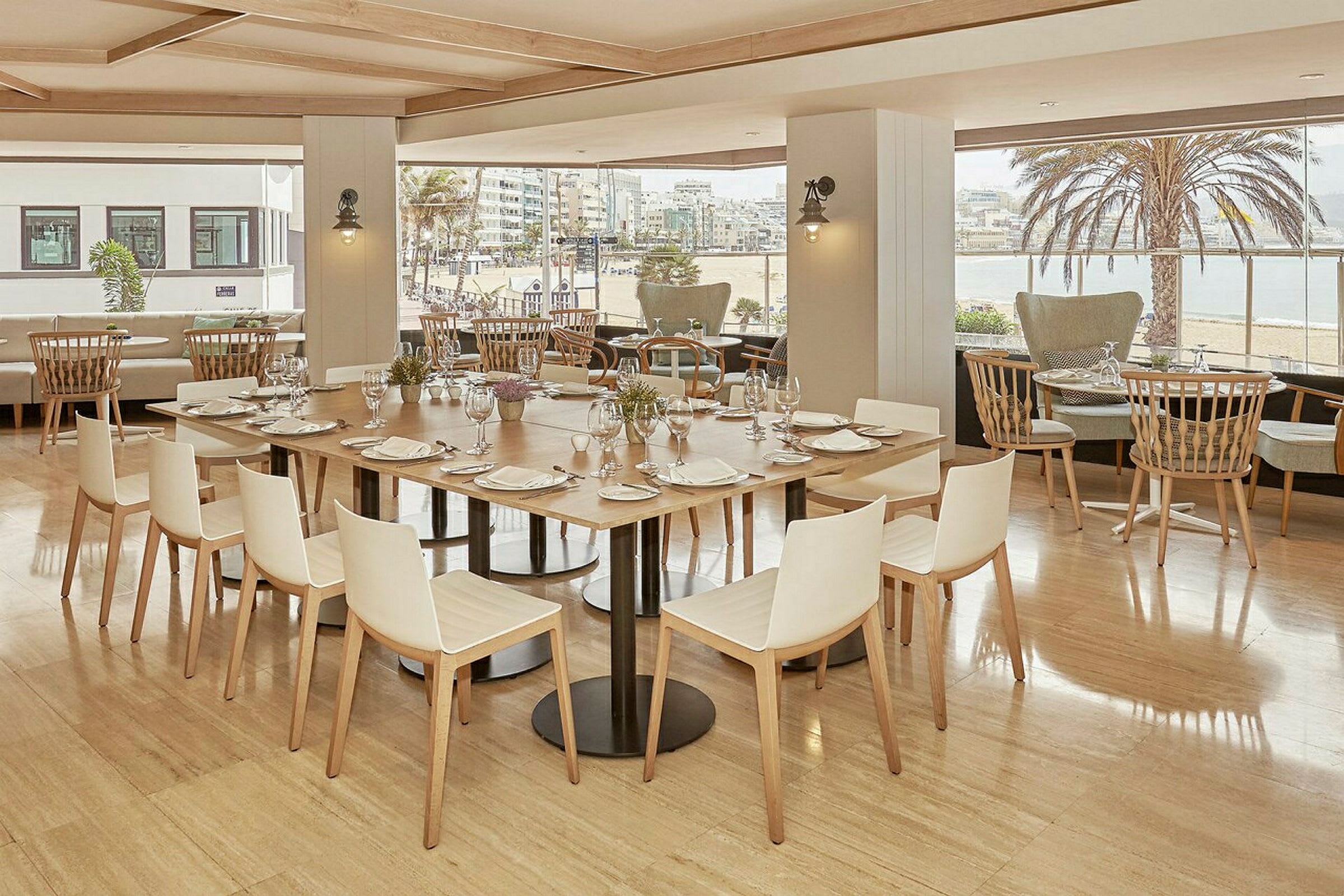 Restaurant med bord dekket med tallerkener og glass. Utsikt mot en strand utenfor vinduene. (AI-generert tekst)