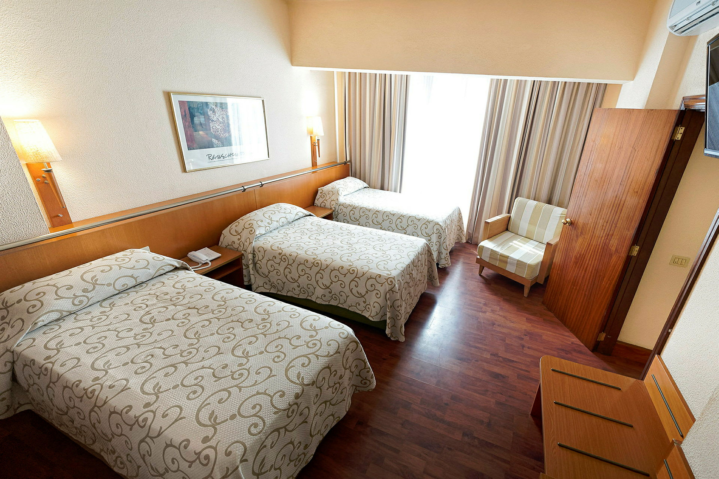 Hotellrom med tre enkeltsenger, en lenestol og tregulv. (AI-generert tekst)