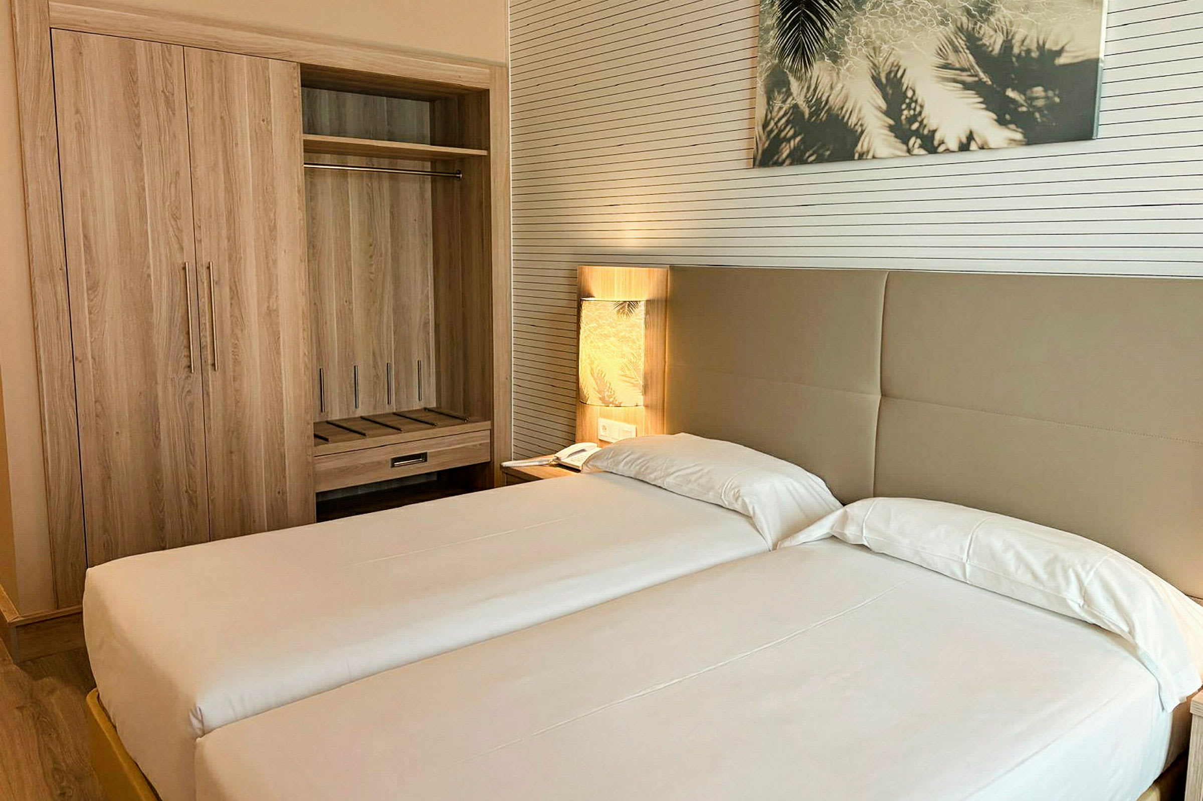 Hotellrom med to enkeltsenger, et garderobeskap og en bordlampe ved siden av sengen. (AI-generert tekst)