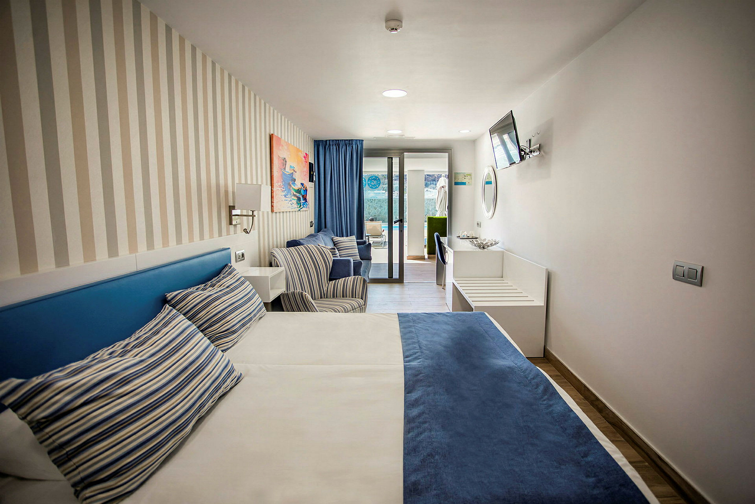 Hotellrom med en seng, to stoler og vindu mot en terrasse. (AI-generert tekst)