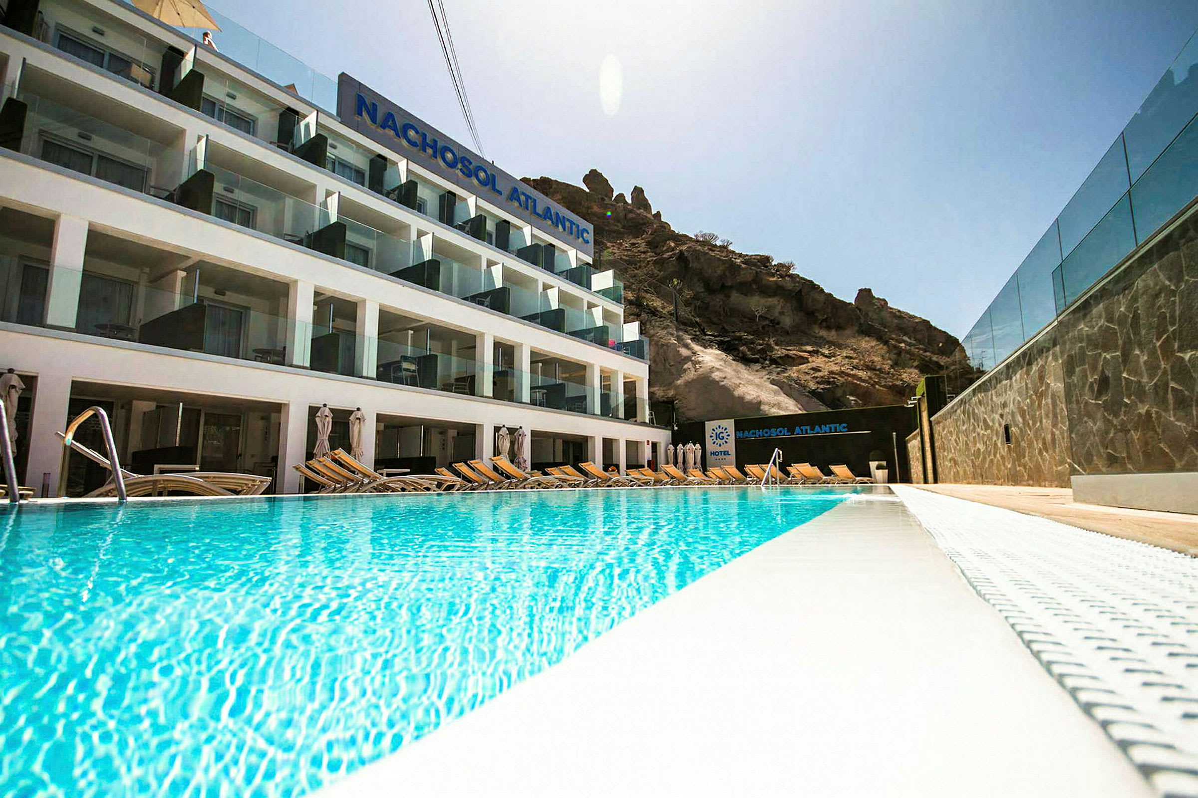 Hotel Nachosol Atlantic med basseng foran og fjell i bakgrunnen. (AI-generert tekst)