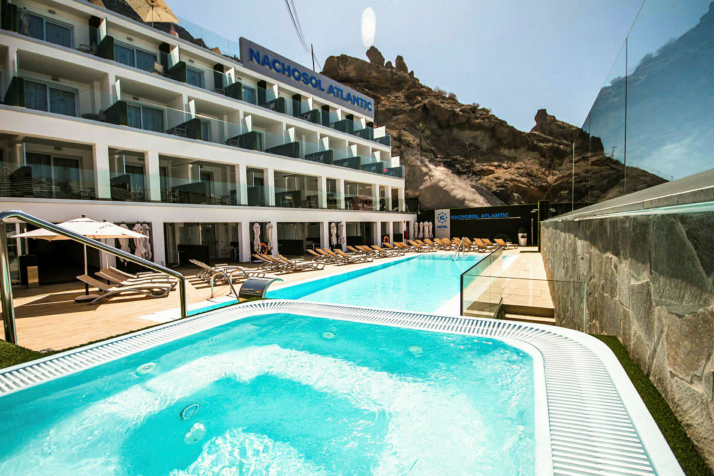 Hotellfasade med basseng og solsenger i forgrunnen. (AI-generert tekst)