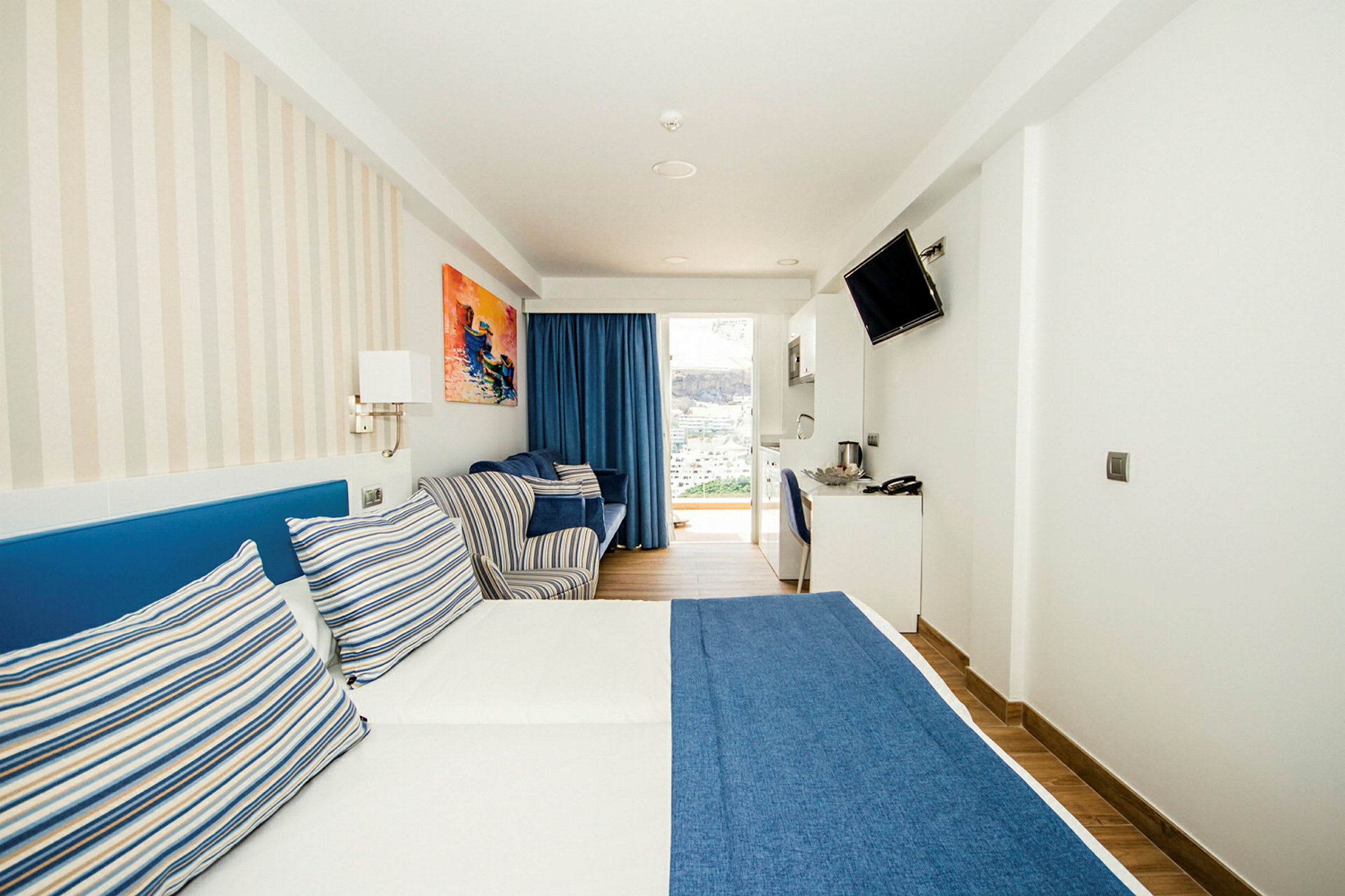 Et hotellrom med en dobbeltseng med blått sengetrekk og stripete puter. (AI-generert tekst)