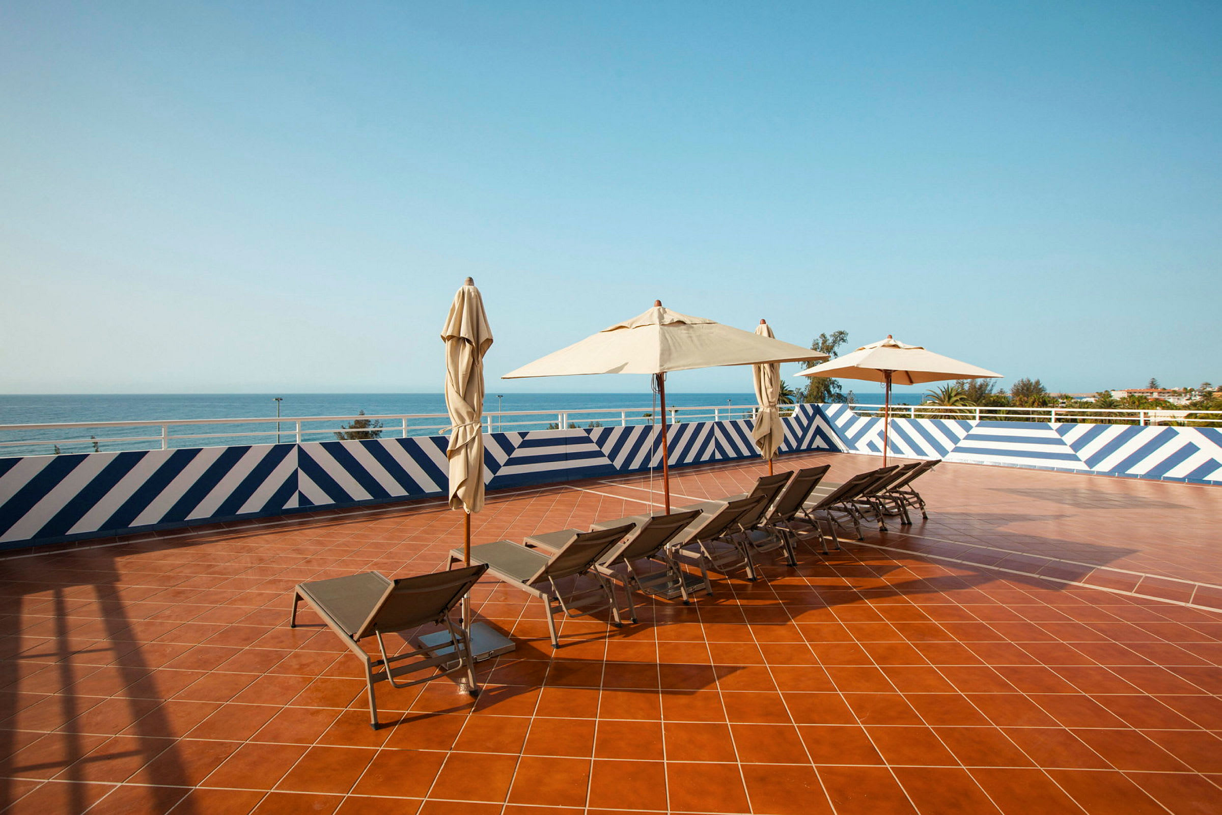 Solterrasse med solsenger og parasoller, utsikt over havet. (AI-generert tekst)