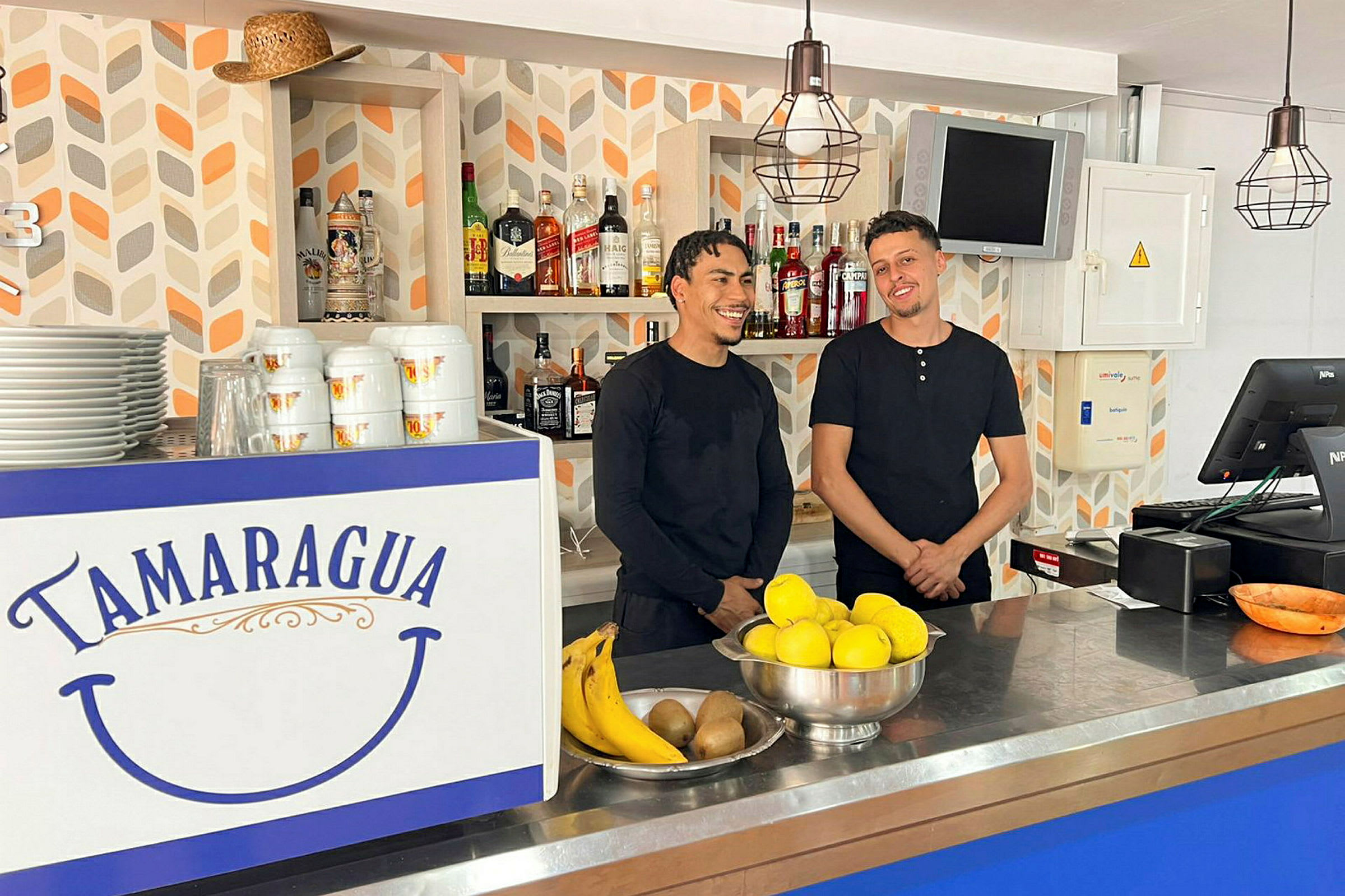 En bar med en disk dekorert med teksten "Tamaragua". På disken er det frukt og servise. Bakgrunnen har hyller med flasker. (AI-generert tekst)