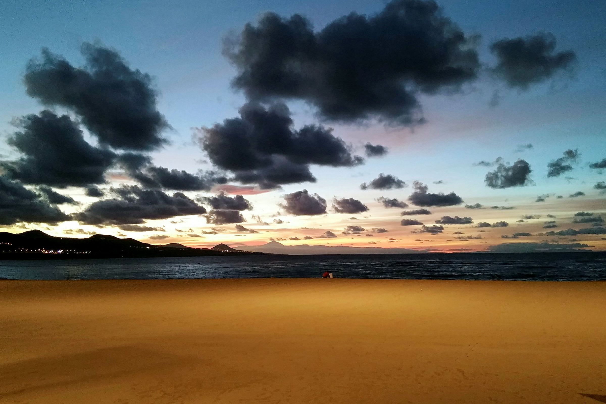 Sandstrand ved havet under en kveldshimmel med skyer og solnedgang. (AI-generert tekst)