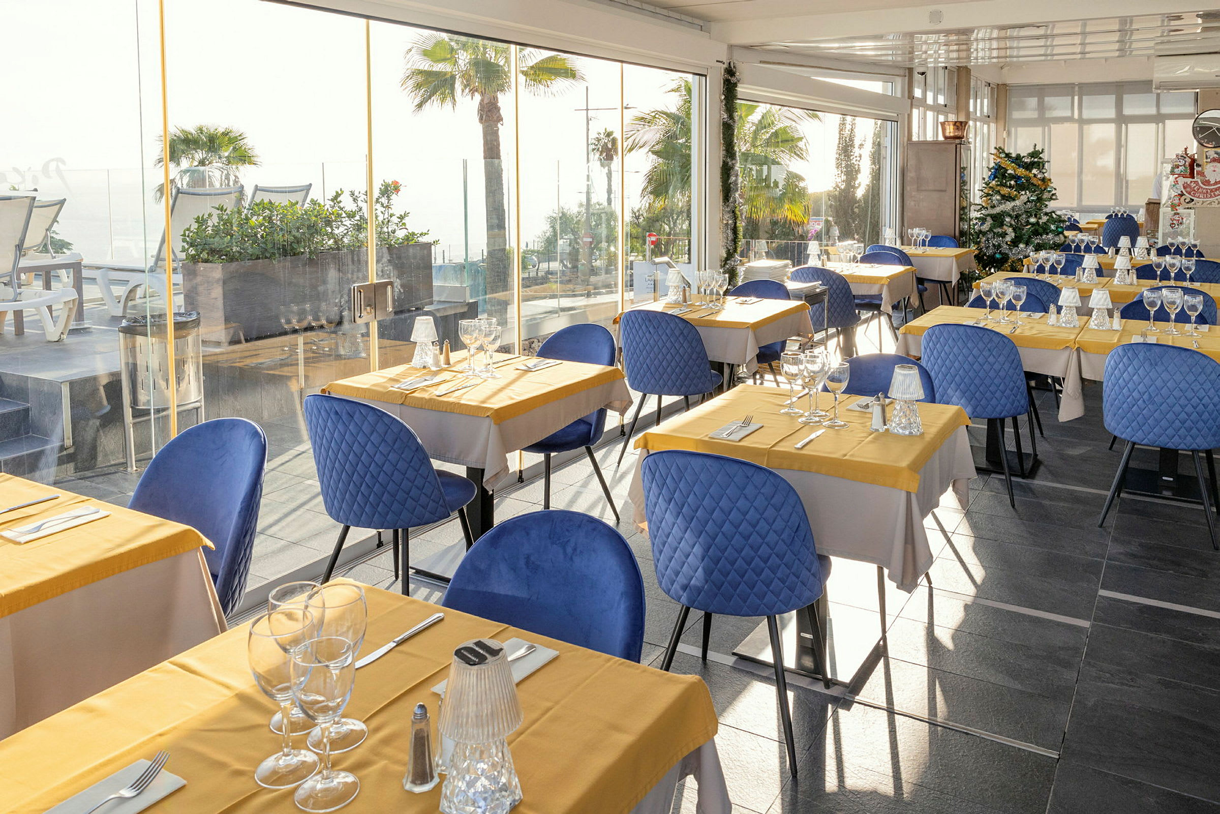 Restaurant med bord dekket med gule duker og blå stoler. (AI-generert tekst)
