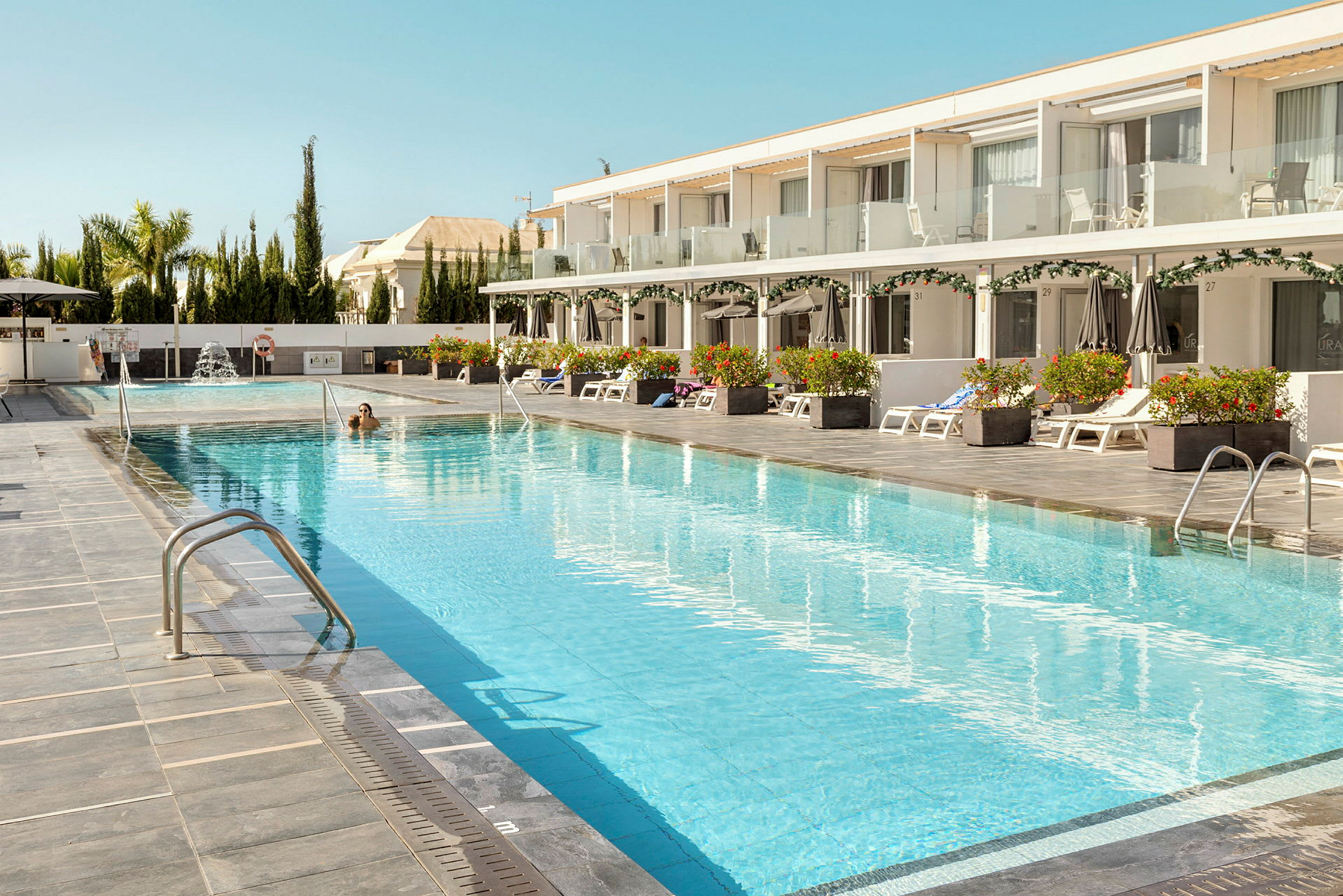 Et hotellbasseng med solsenger og parasoller på siden. (AI-generert tekst)