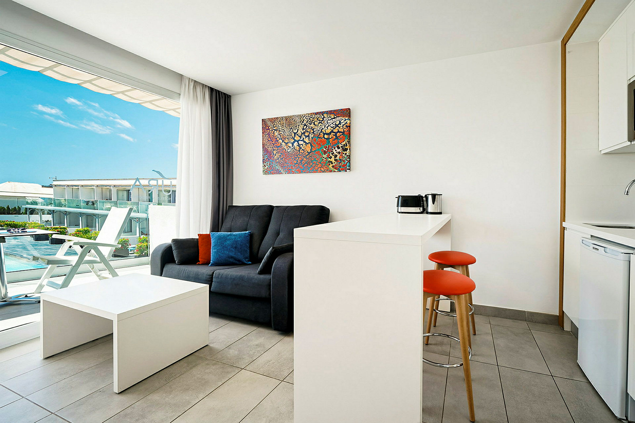 Et moderne hotellrom med sofa, bord, tekjøkken og en balkong med utsikt. (AI-generert tekst)