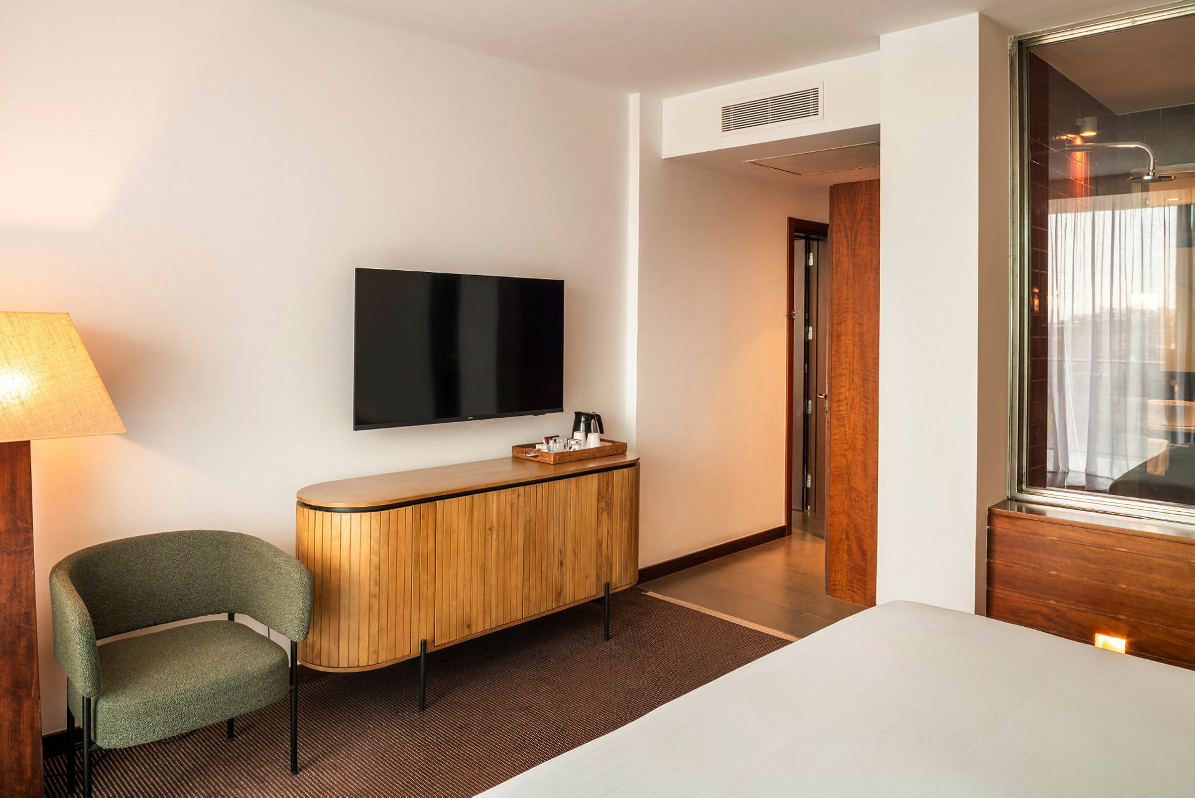 Et hotellrom med beige vegger, en dreibar stol, en elegant TV montert på veggen over en tregarderobe og en dør som fører til badet. (AI-generert tekst)