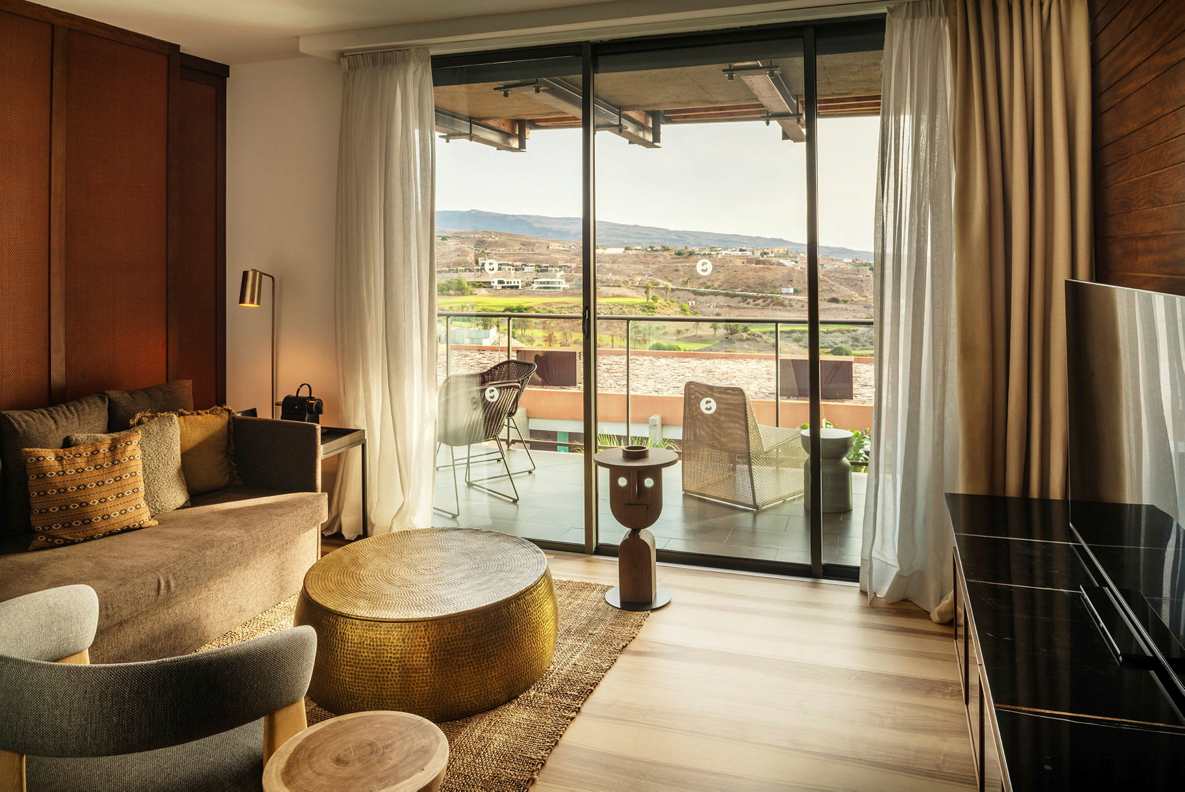 En innredet hotellsuite med en sittegruppe og utsikt mot en balkong og landskap. (AI-generert tekst)