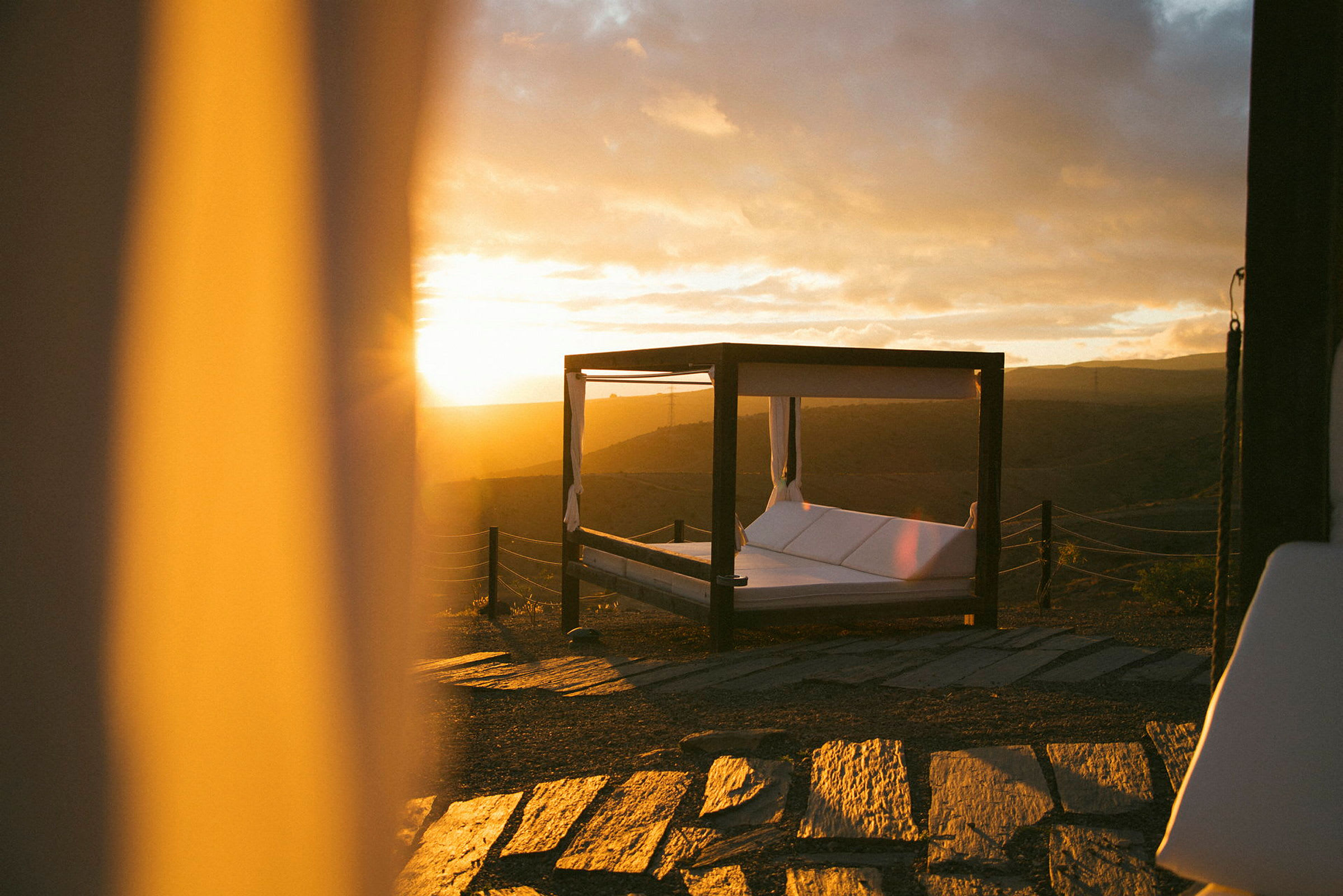 En himmelseng på en terrasse med solnedgang i bakgrunnen. (AI-generert tekst)