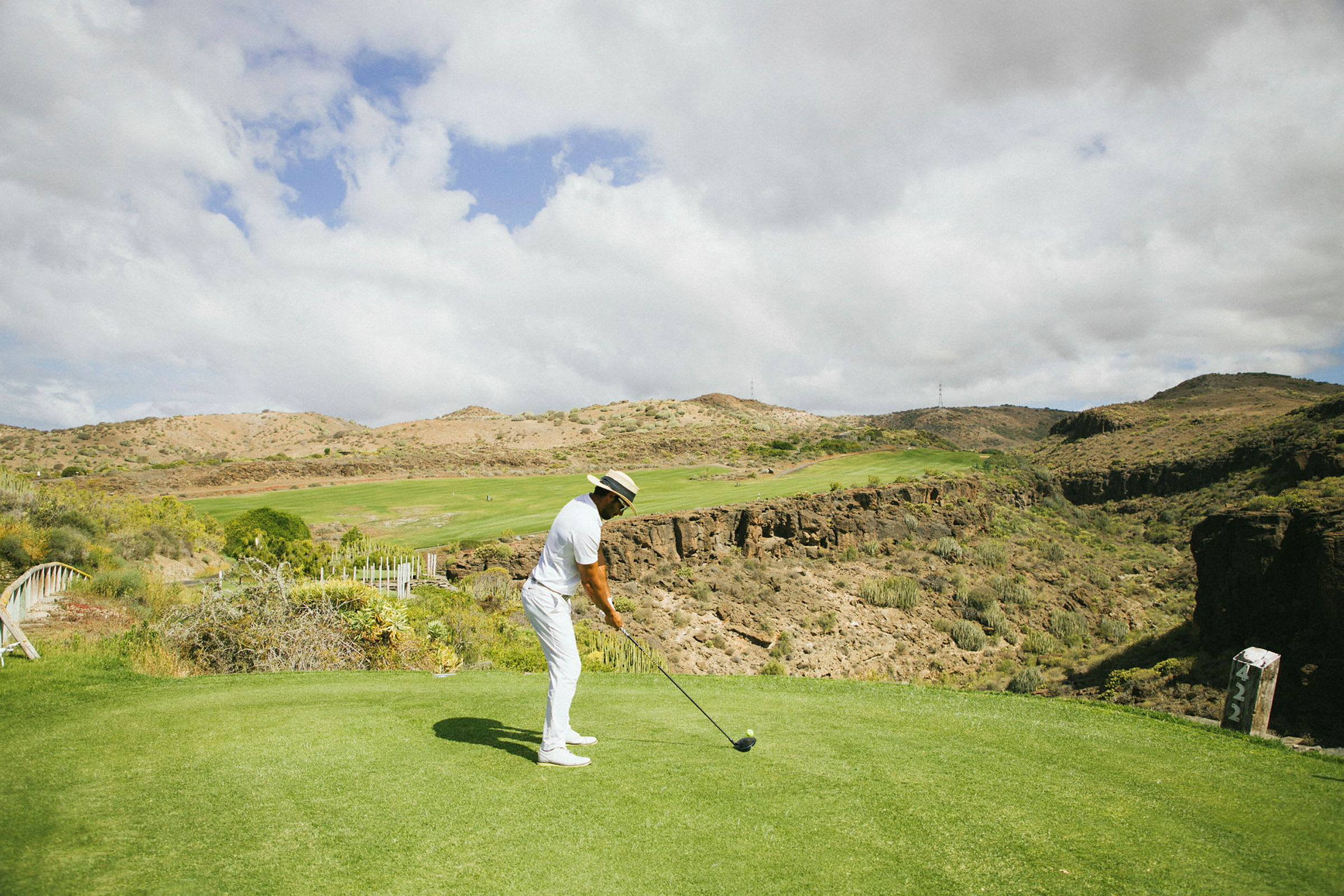 En person spiller golf på en fjellendt bane under en skyet himmel. (AI-generert tekst)