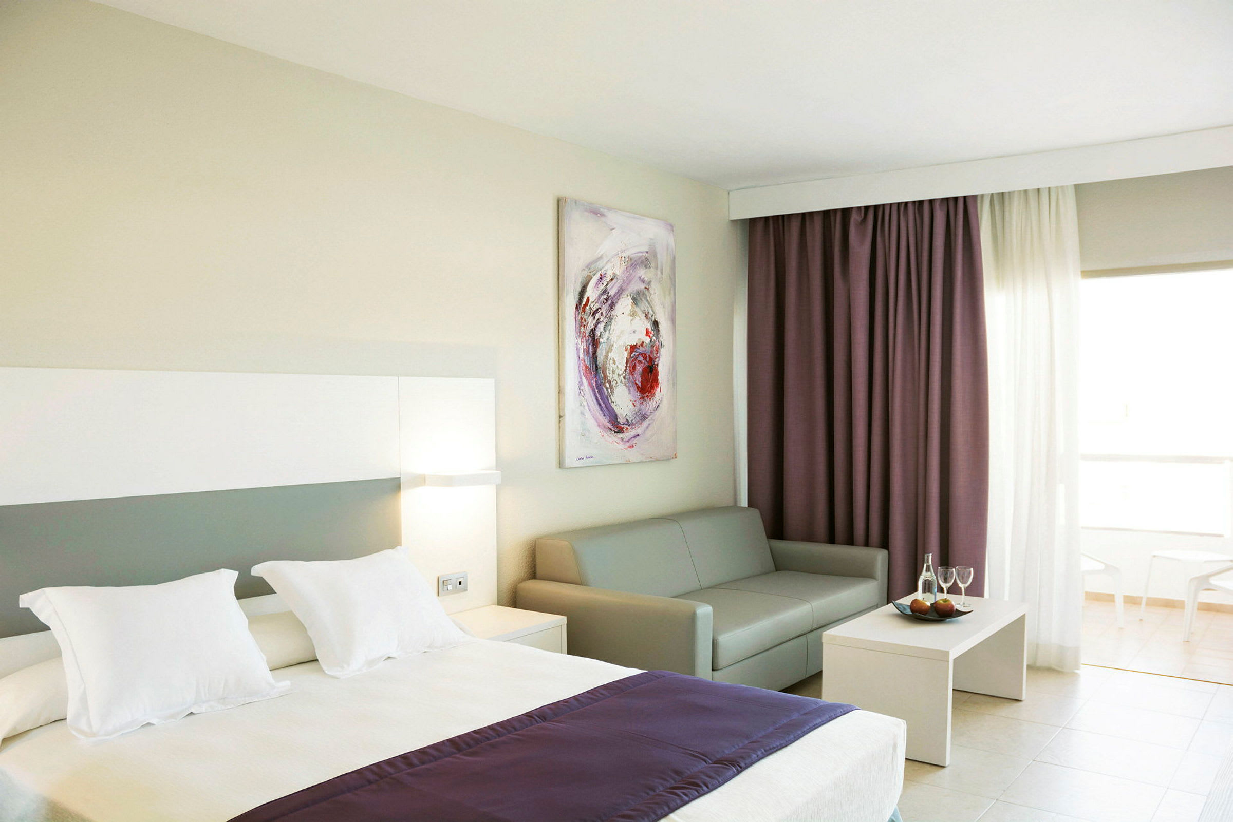 Hotellrom med seng, sofa, sofabord og gardiner. (AI-generert tekst)