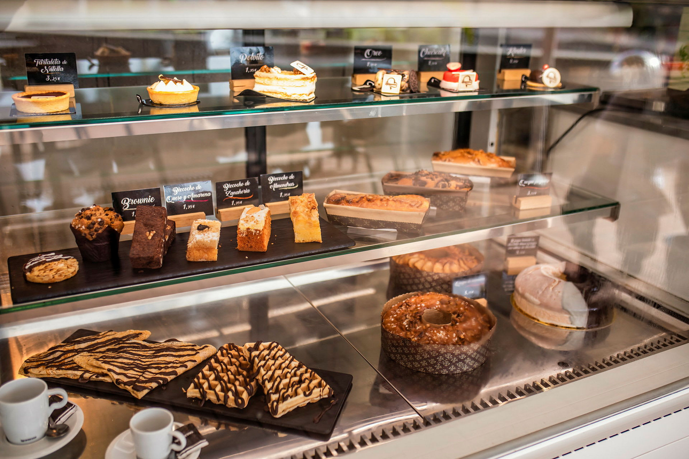 Et kjøleskap med forskjellige bakverk og desserter, inkludert muffins, kaker og terter, plassert på hyller. (AI-generert tekst)