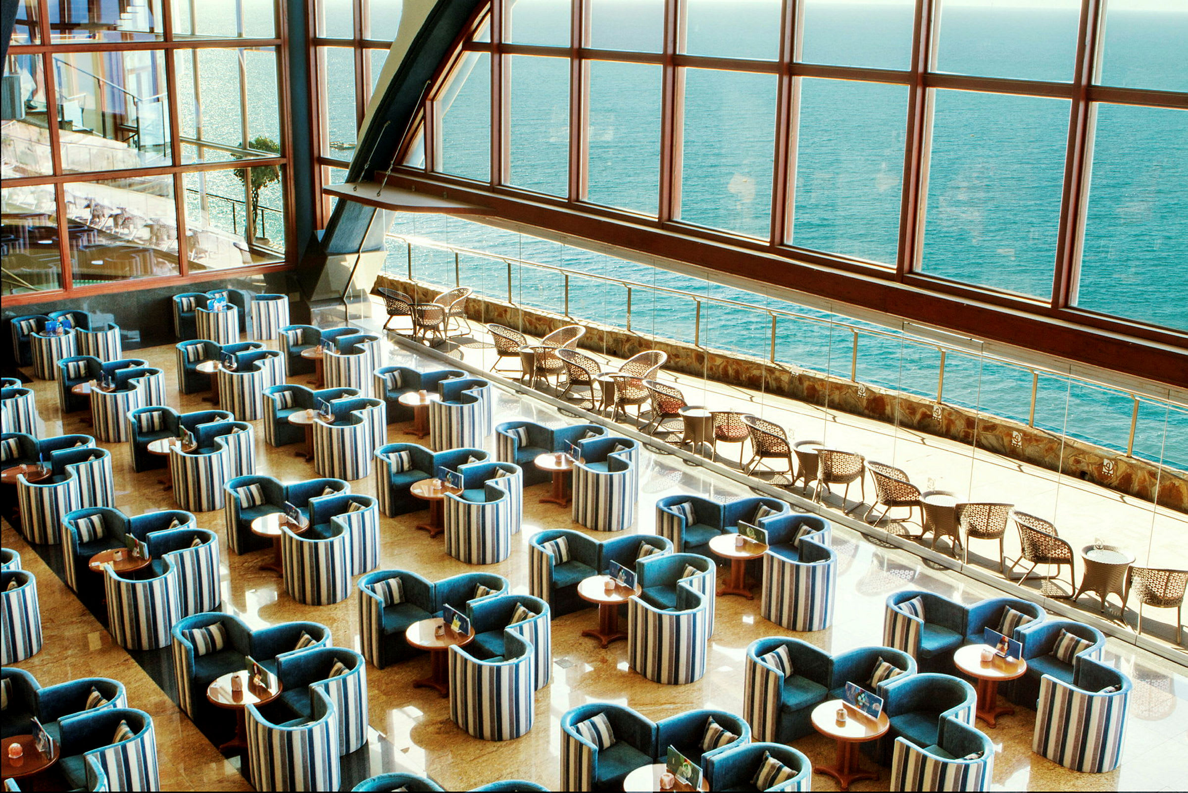 En innendørs lounge med organiserte sitteplasser og stor vindusutsikt mot havet. (AI-generert tekst)