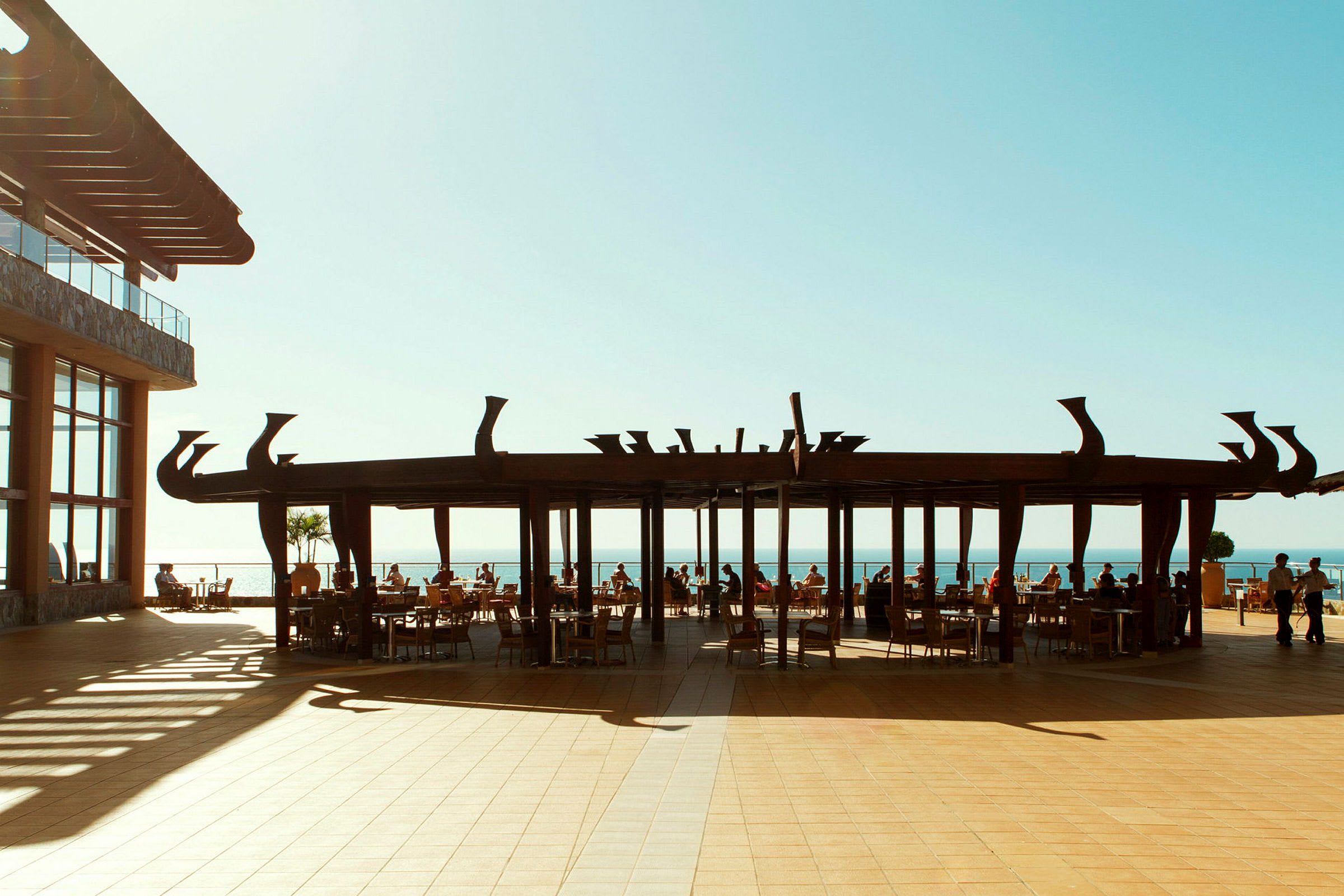 En utendørs restaurant med havutsikt under en stilisert pergola. (AI-generert tekst)
