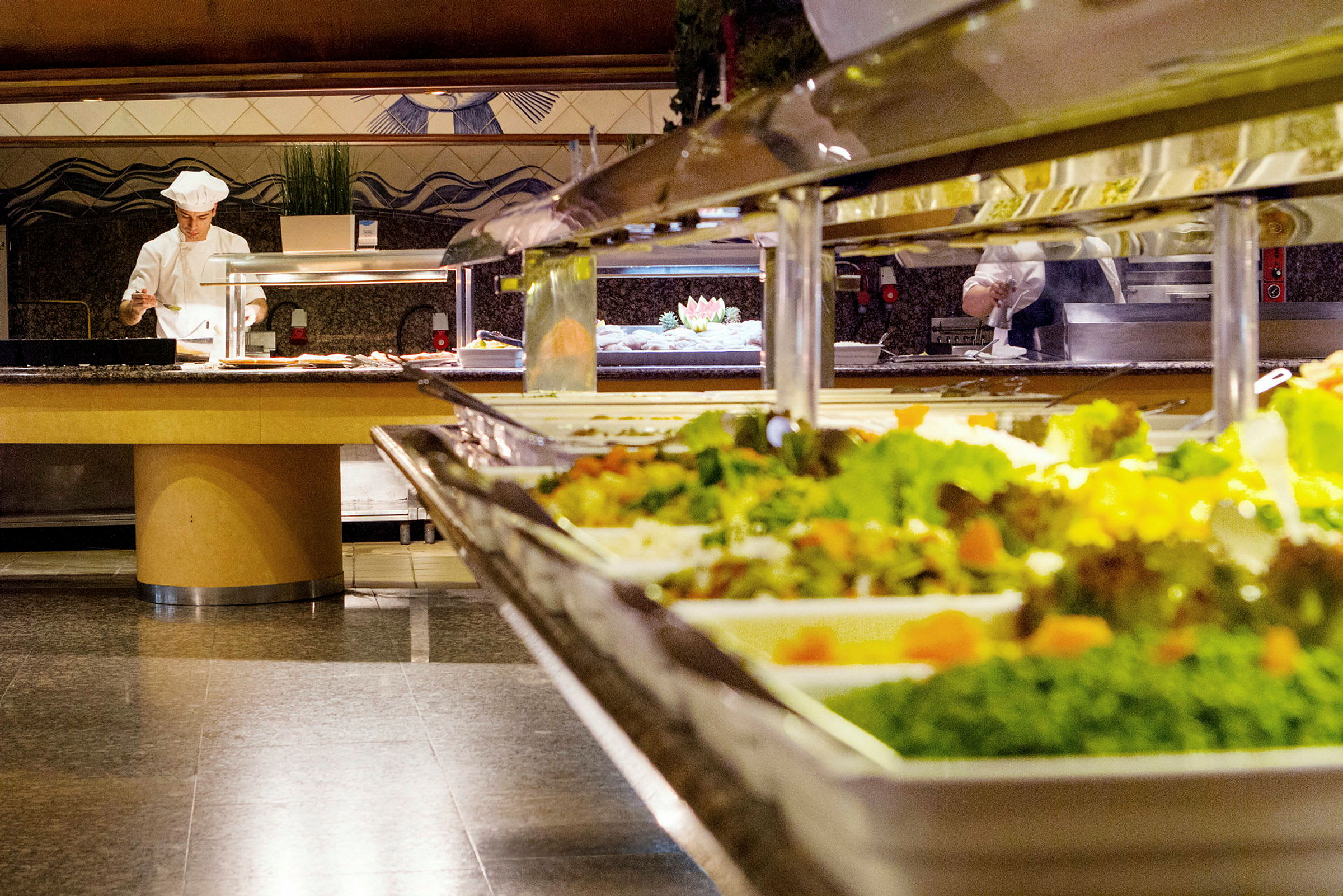 Buffetbord med salater og en kokk som tilbereder mat i bakgrunnen. (AI-generert tekst)