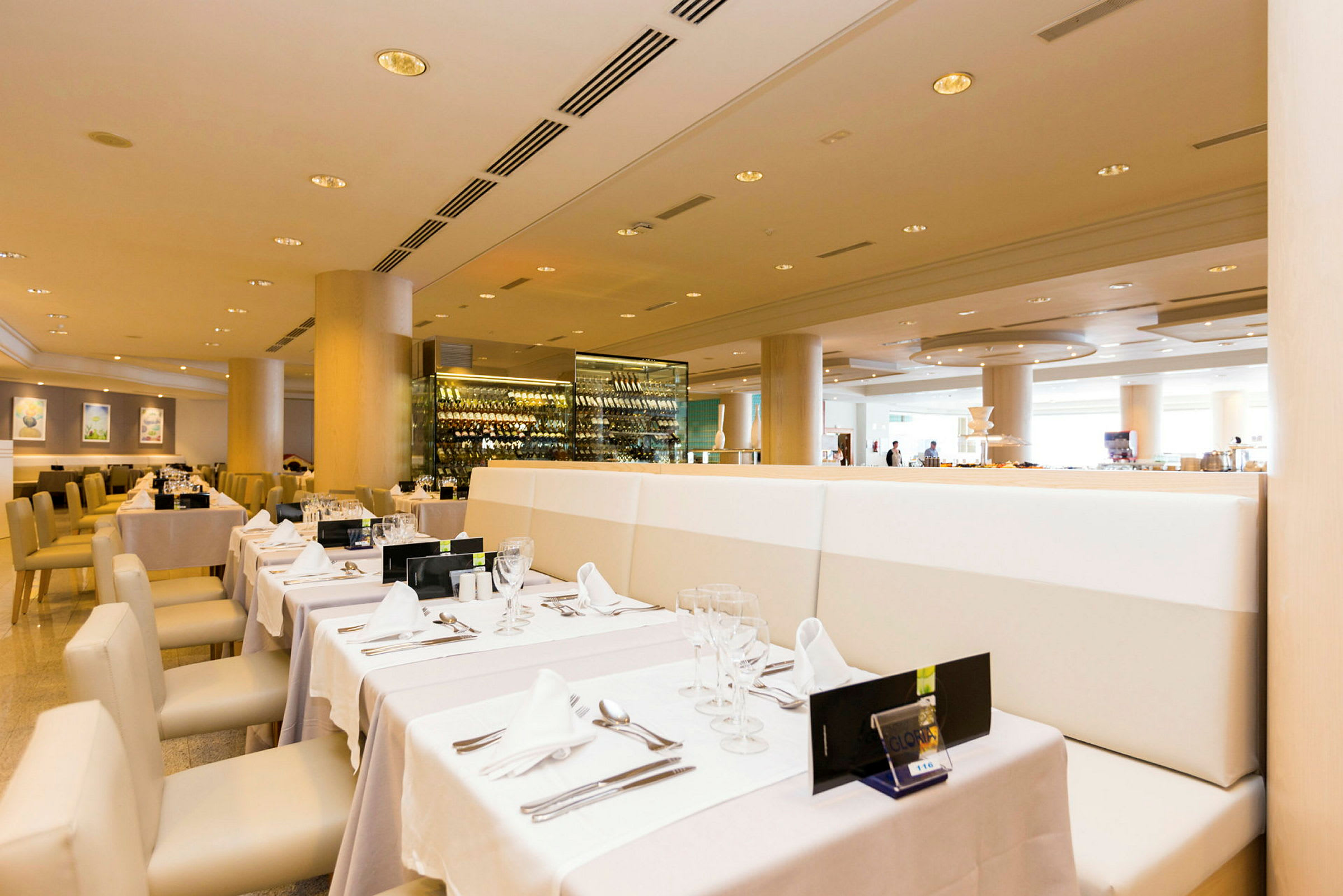 En restaurant med elegante bord dekket med hvite duker og glass. En vinoppbevaring vises i bakgrunnen. (AI-generert tekst)