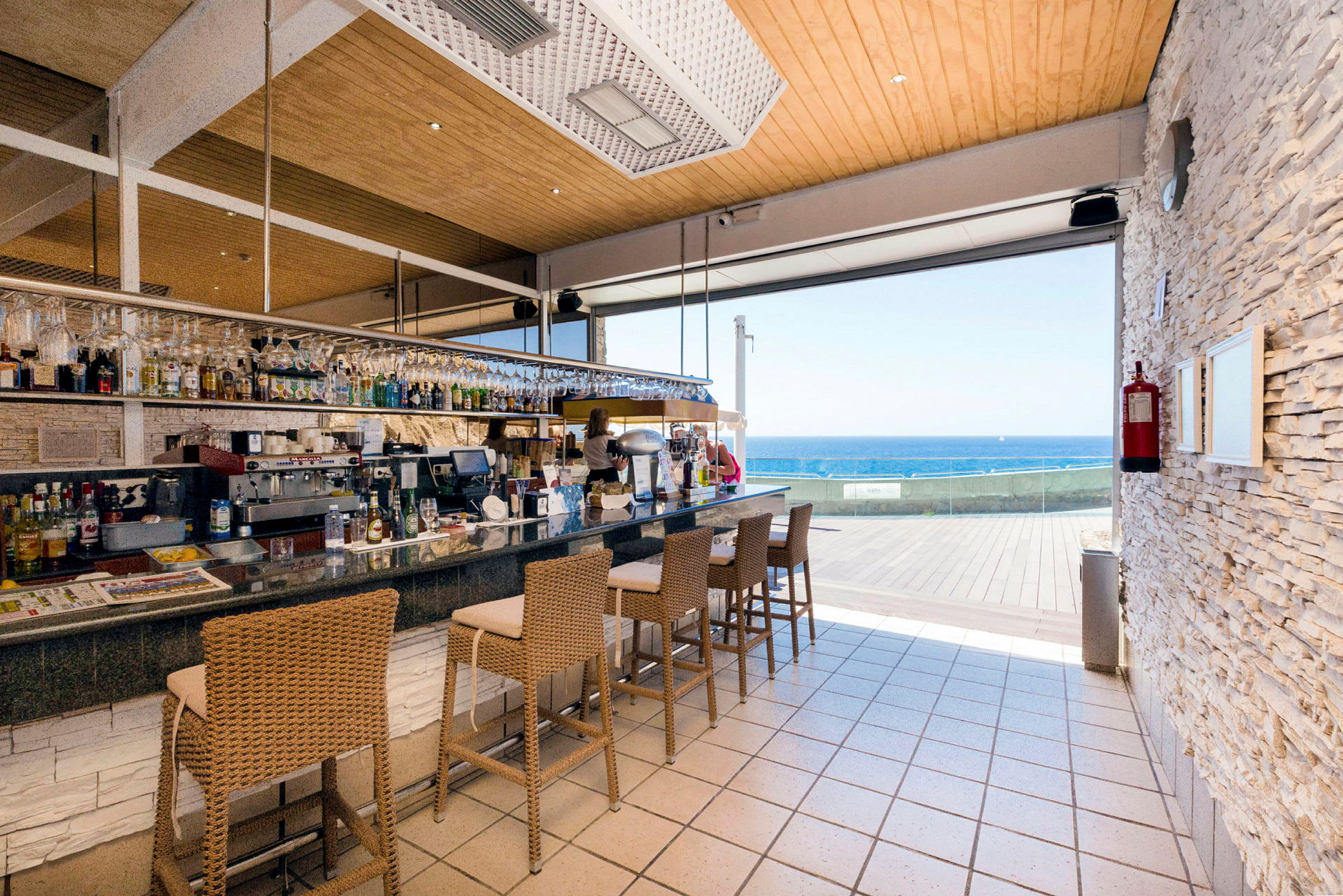 En bar med høye stoler og utsikt over havet. (AI-generert tekst)