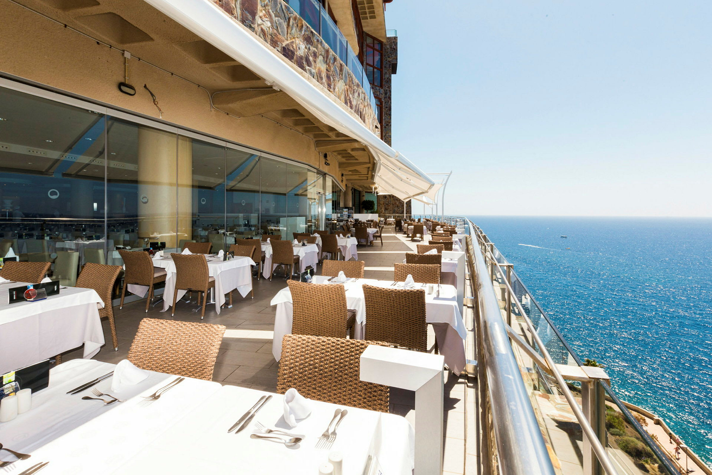 Restaurant med bord og stoler på en terrasse med utsikt over havet. (AI-generert tekst)