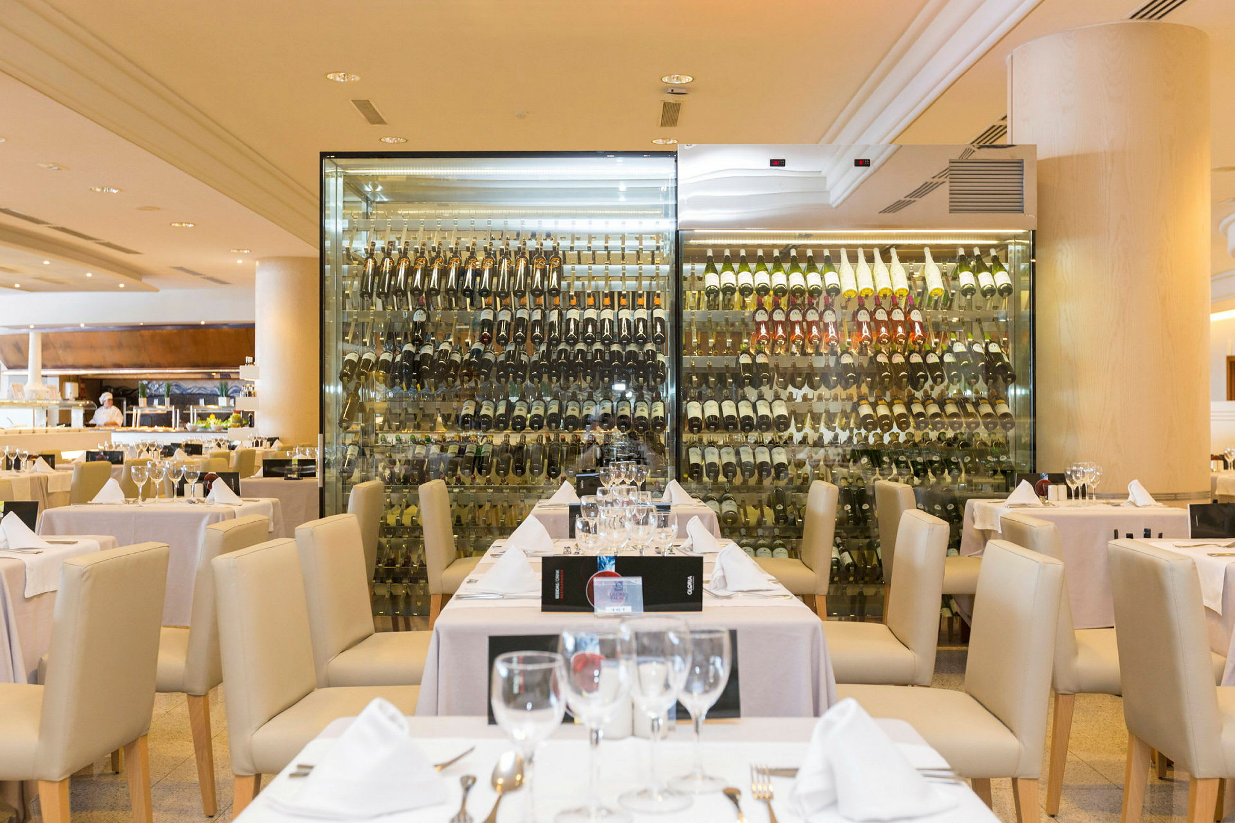 En restaurant med dekket bord foran en glassvegg med en samling vinflasker. (AI-generert tekst)