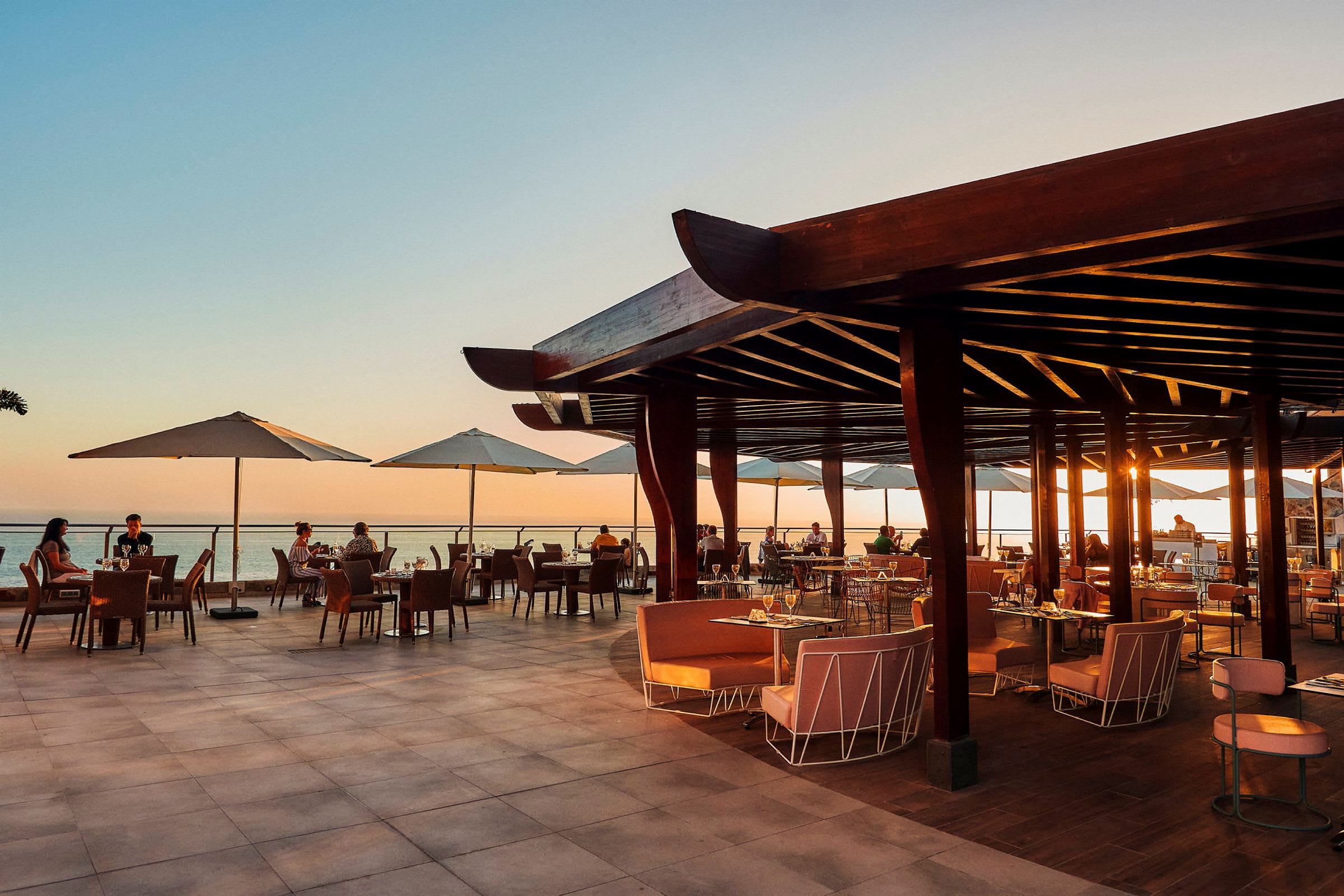 Åpen restaurantterrasse med utsikt over havet ved solnedgang. (AI-generert tekst)