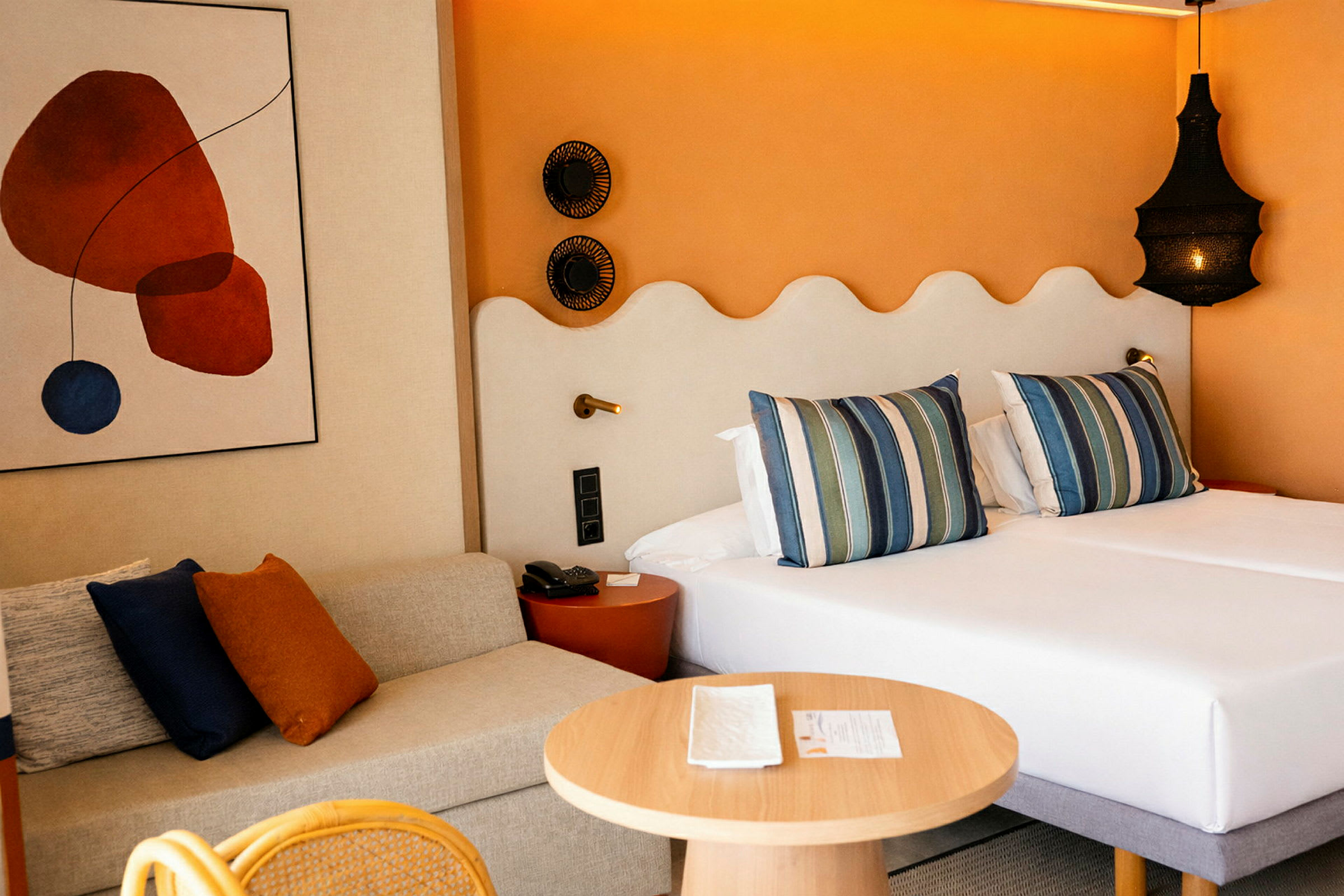 Et hotellrom med to senger, ved siden av en sofa og et rundt trebord. (AI-generert tekst)