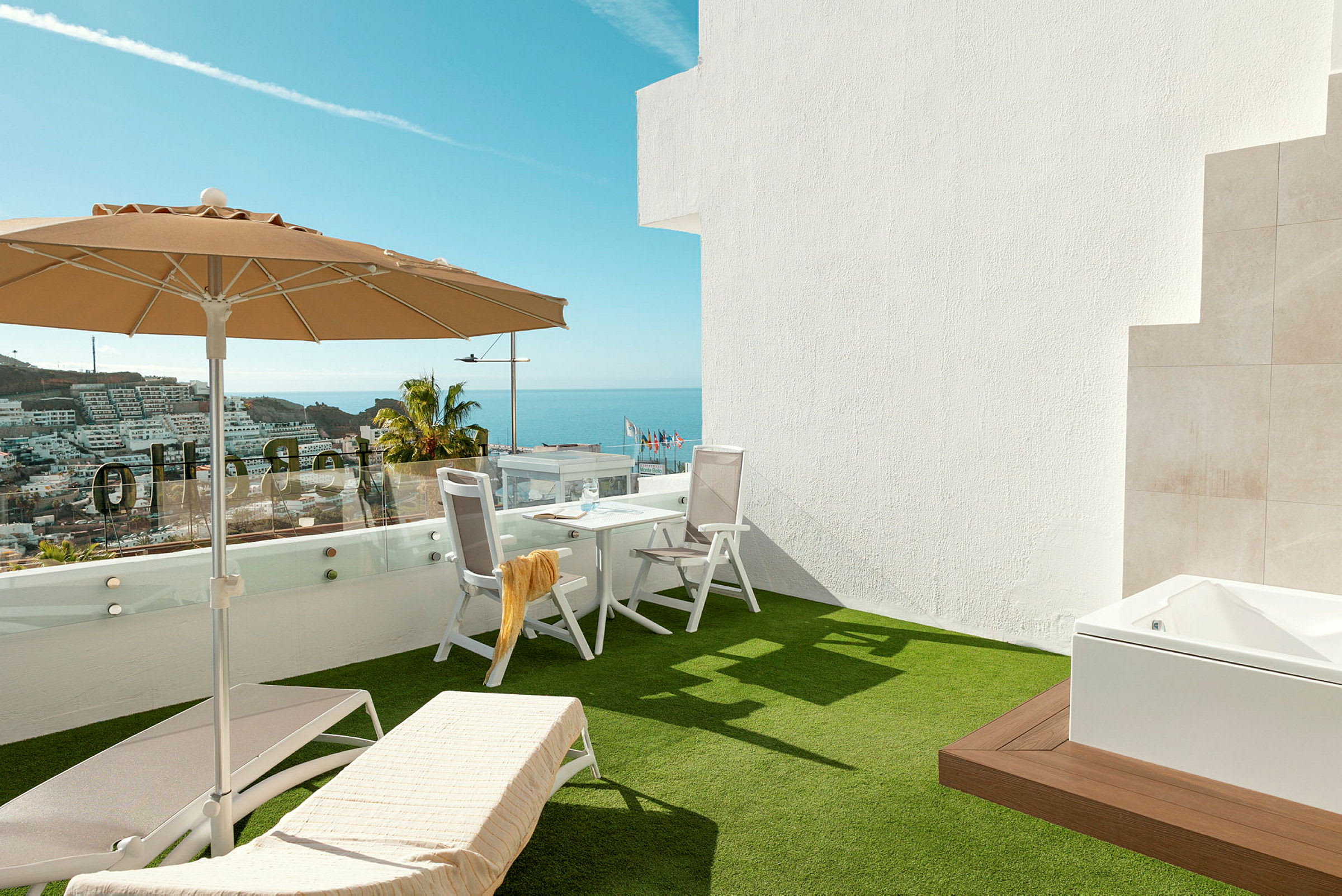 Terrasse med solsenger, parasoll og bord med stoler, havutsikt i bakgrunnen. (AI-generert tekst)