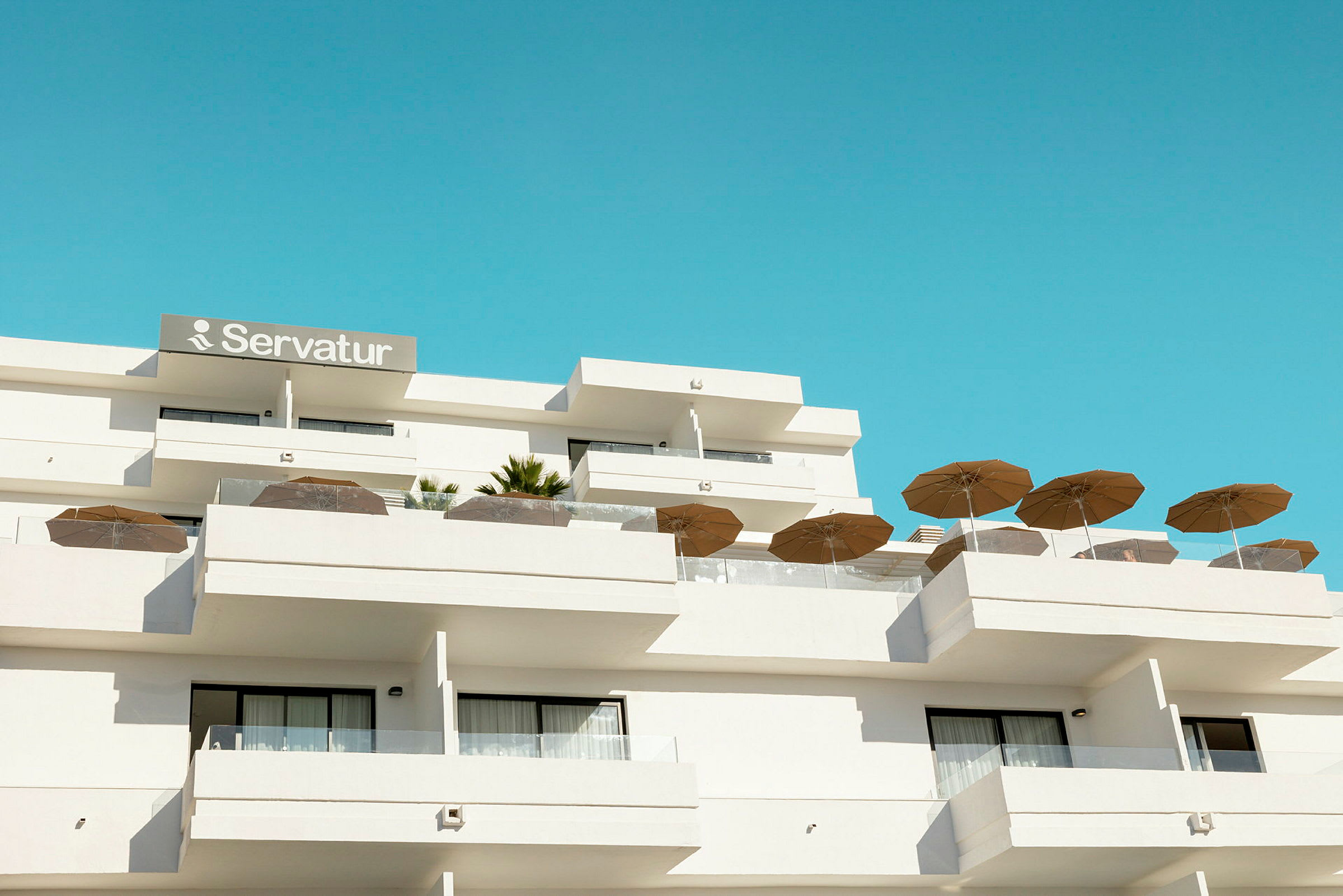 Hotellbygning med balkonger og parasoller mot en blå himmel. (AI-generert tekst)