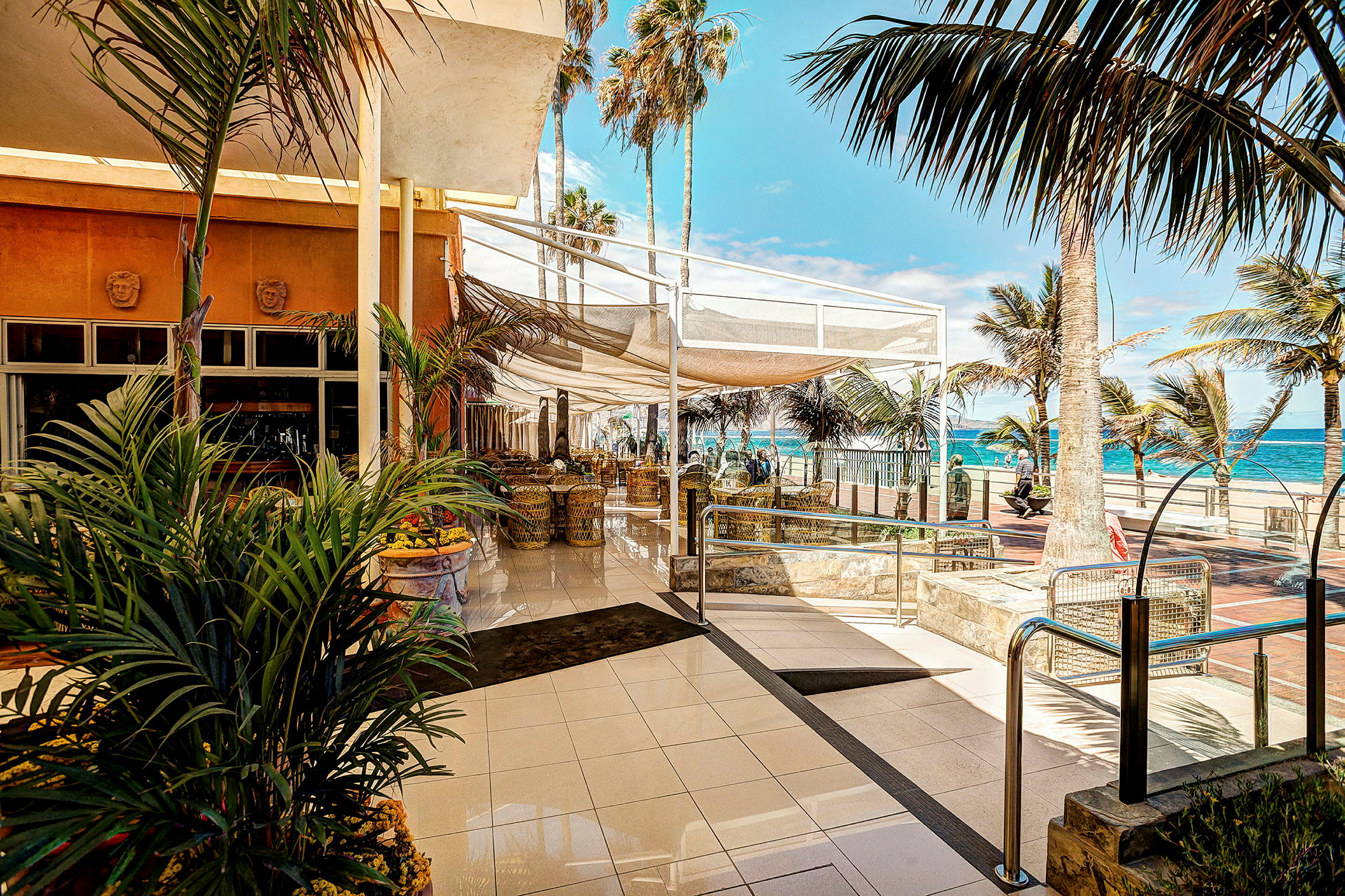 Restaurant ved strandpromenade med palmer og hav i bakgrunnen. (AI-generert tekst)