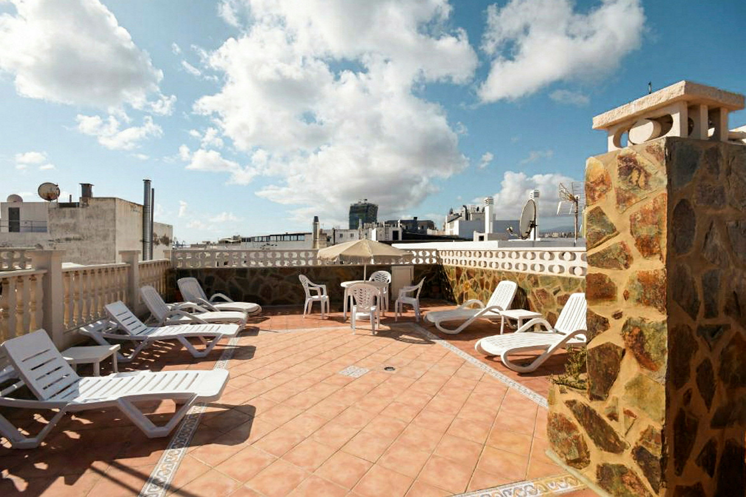 Solstoler og et bord med stoler på en terrasse med utsikt over bygninger. (AI-generert tekst)