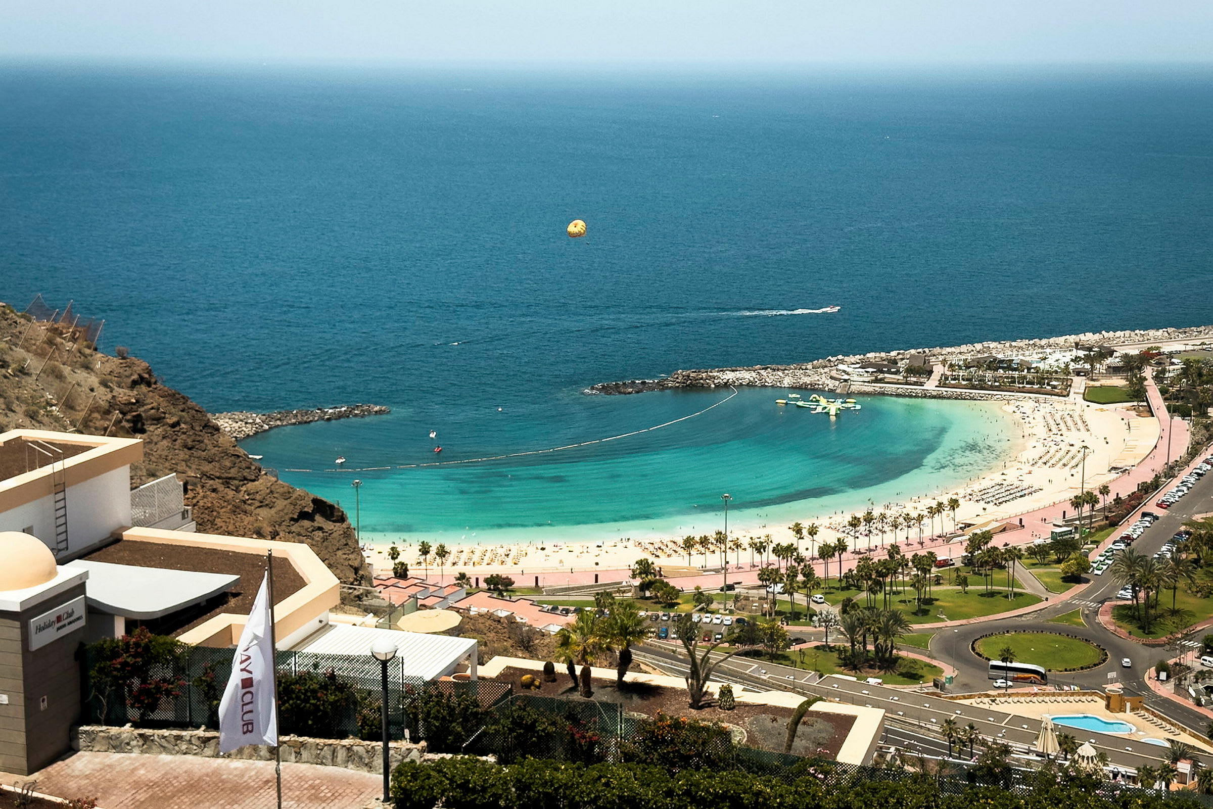 Utsikt over en strand med turkist vann, solsenger og parasoller samt hotellbygninger. (AI-generert tekst)