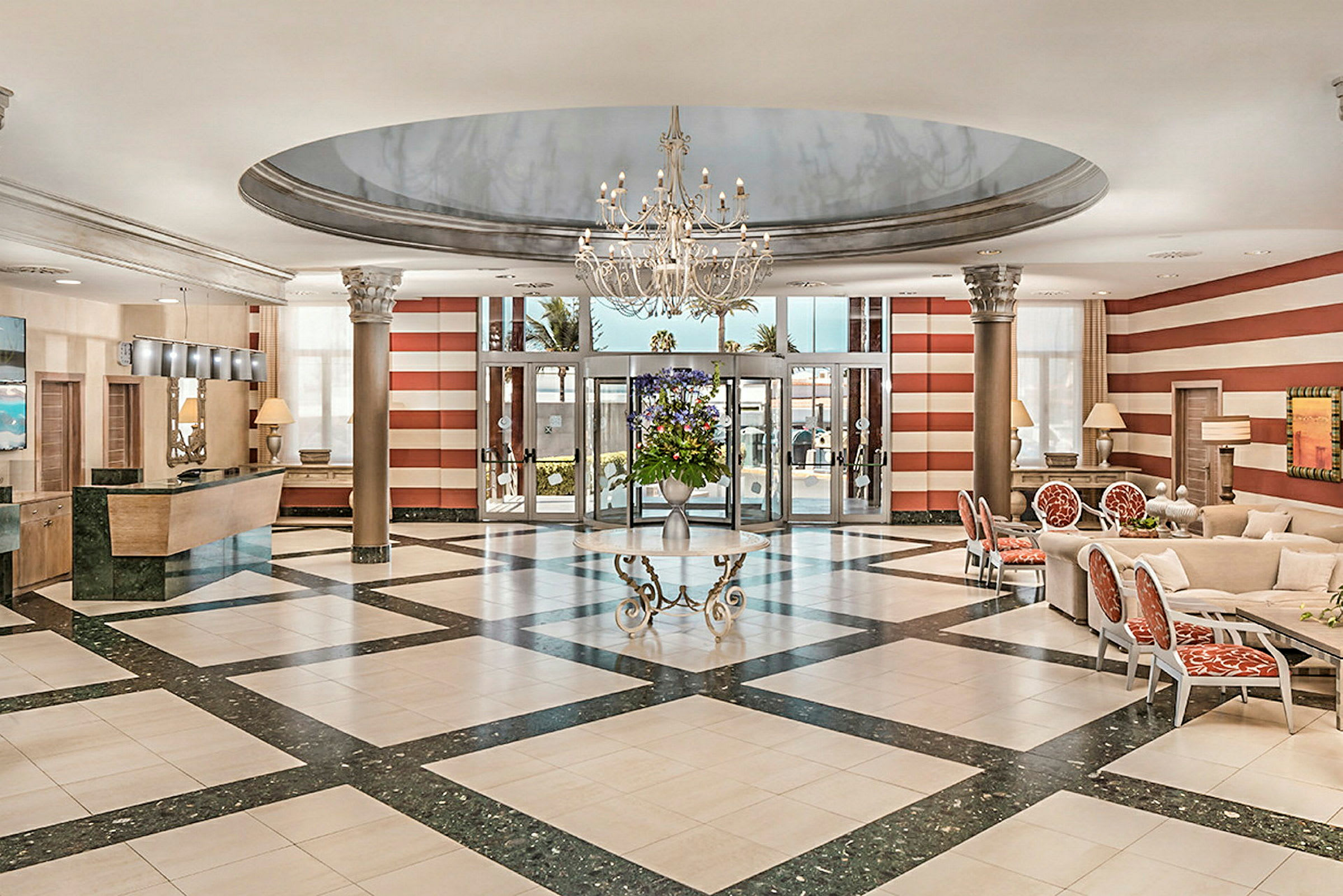Et elegant hotellobbyområde med en lysekrone, marmorgulv, resepsjon til venstre og sitteplasser til høyre. (AI-generert tekst)