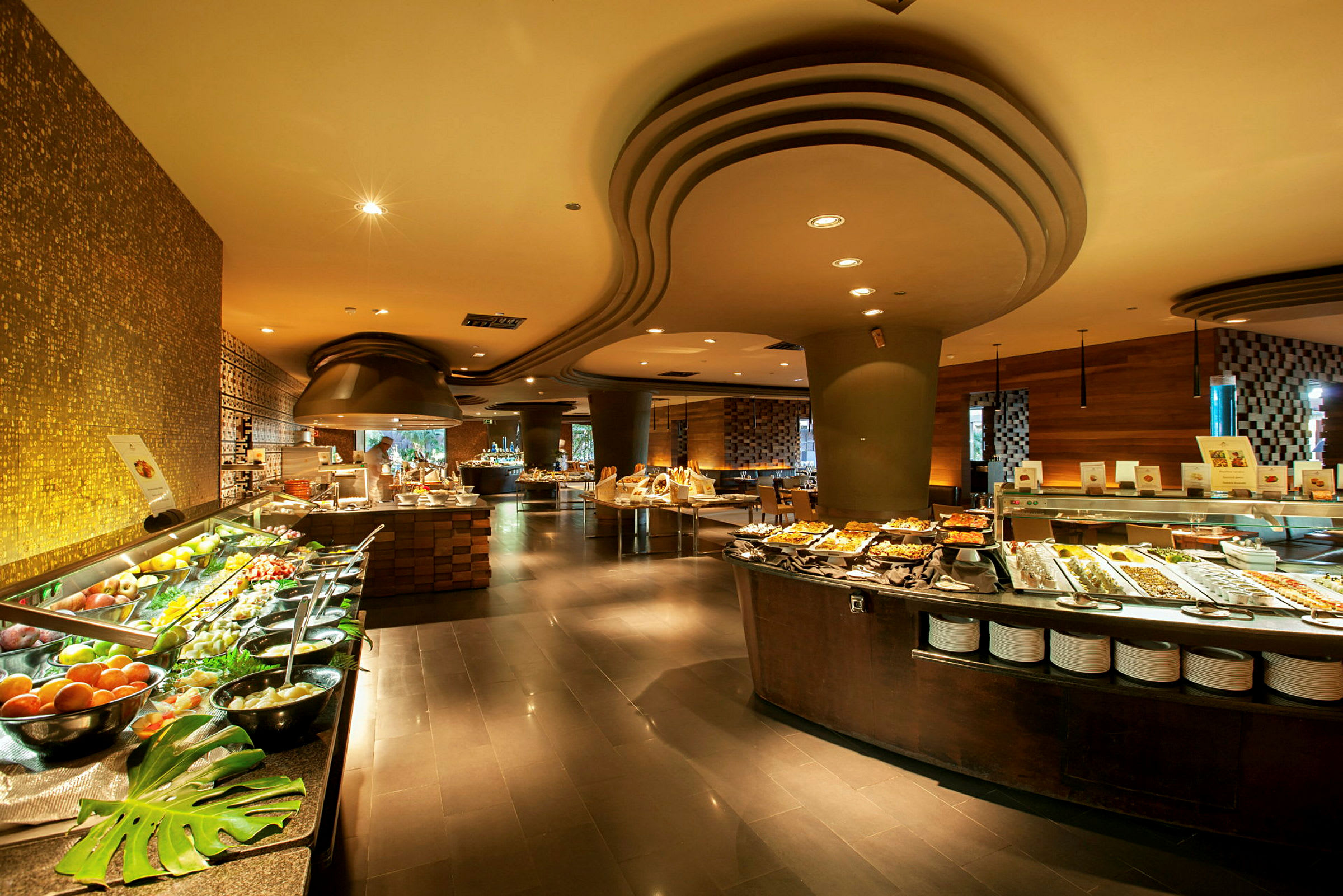 En romslig buffet med forskjellige retter og salater oppstilt på lange bord, omgitt av moderne interiør og stemningsfull belysning. (AI-generert tekst)