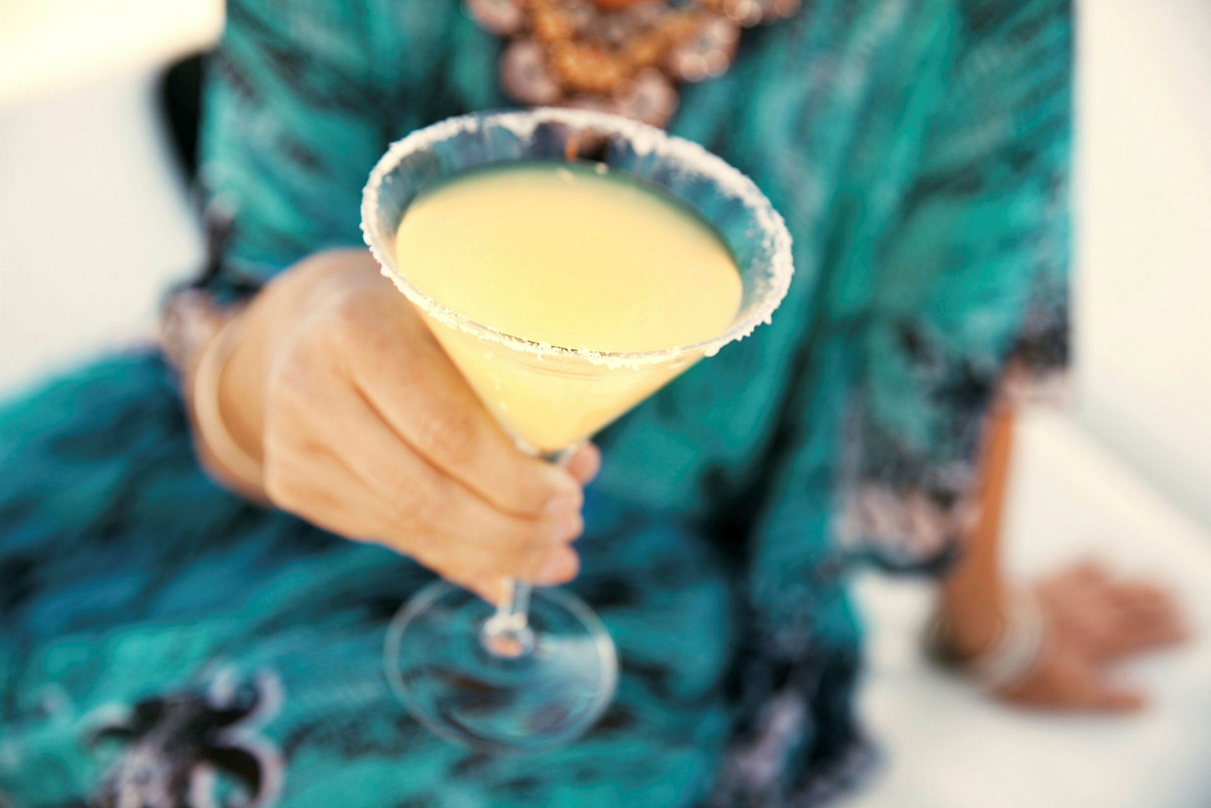 En person holder et cocktailglass fylt med gul drikke og dekorert med sukkerkant. (AI-generert tekst)