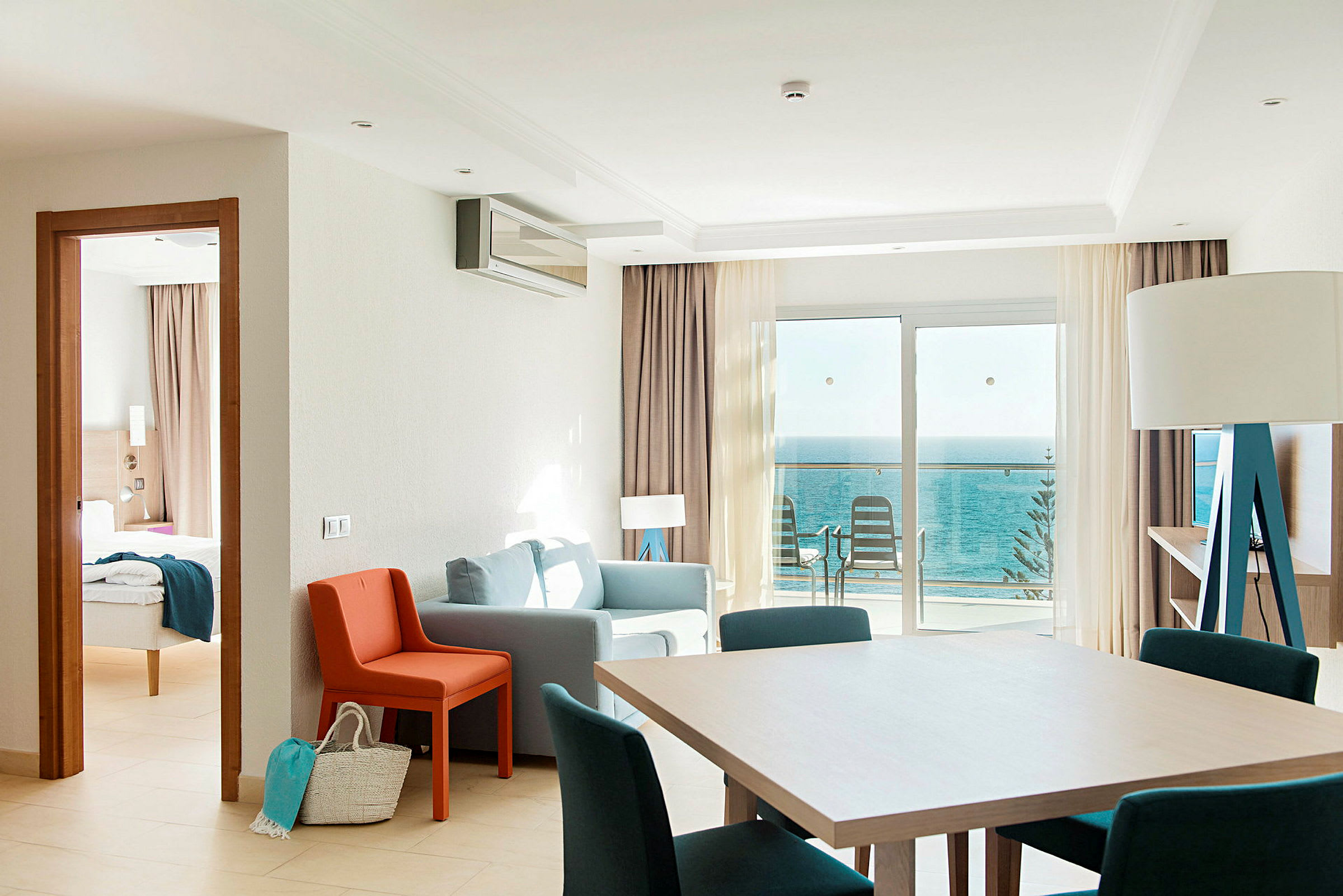 Et hotellrom med sittegruppe, spisebord og havutsikt fra balkongen. (AI-generert tekst)