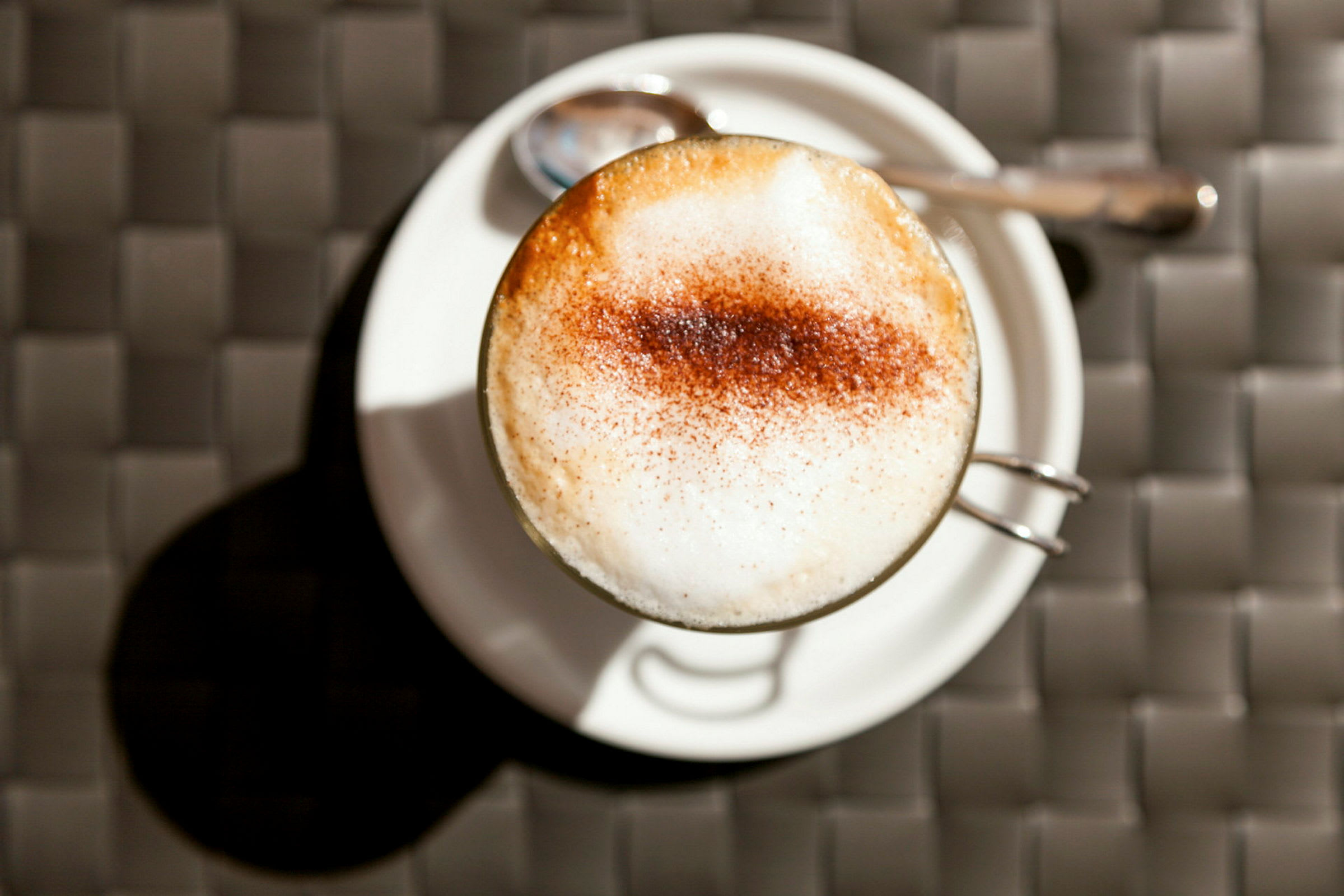 En kopp cappuccino på en hvit tallerken med en skje ved siden av. (AI-generert tekst)