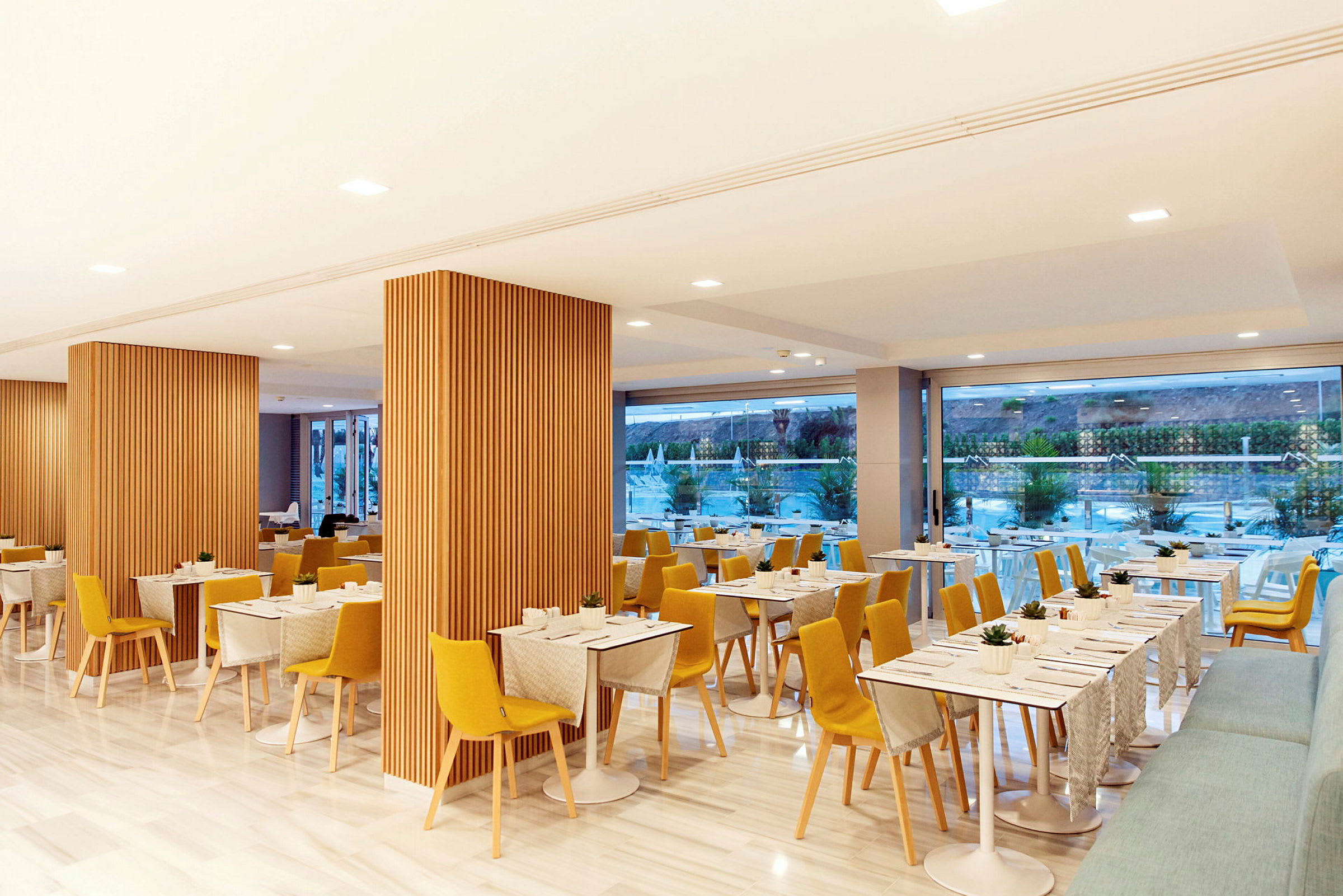 Bilde av en moderne restaurant med trematerialer, gule stoler og bord med duker. (AI-generert tekst)