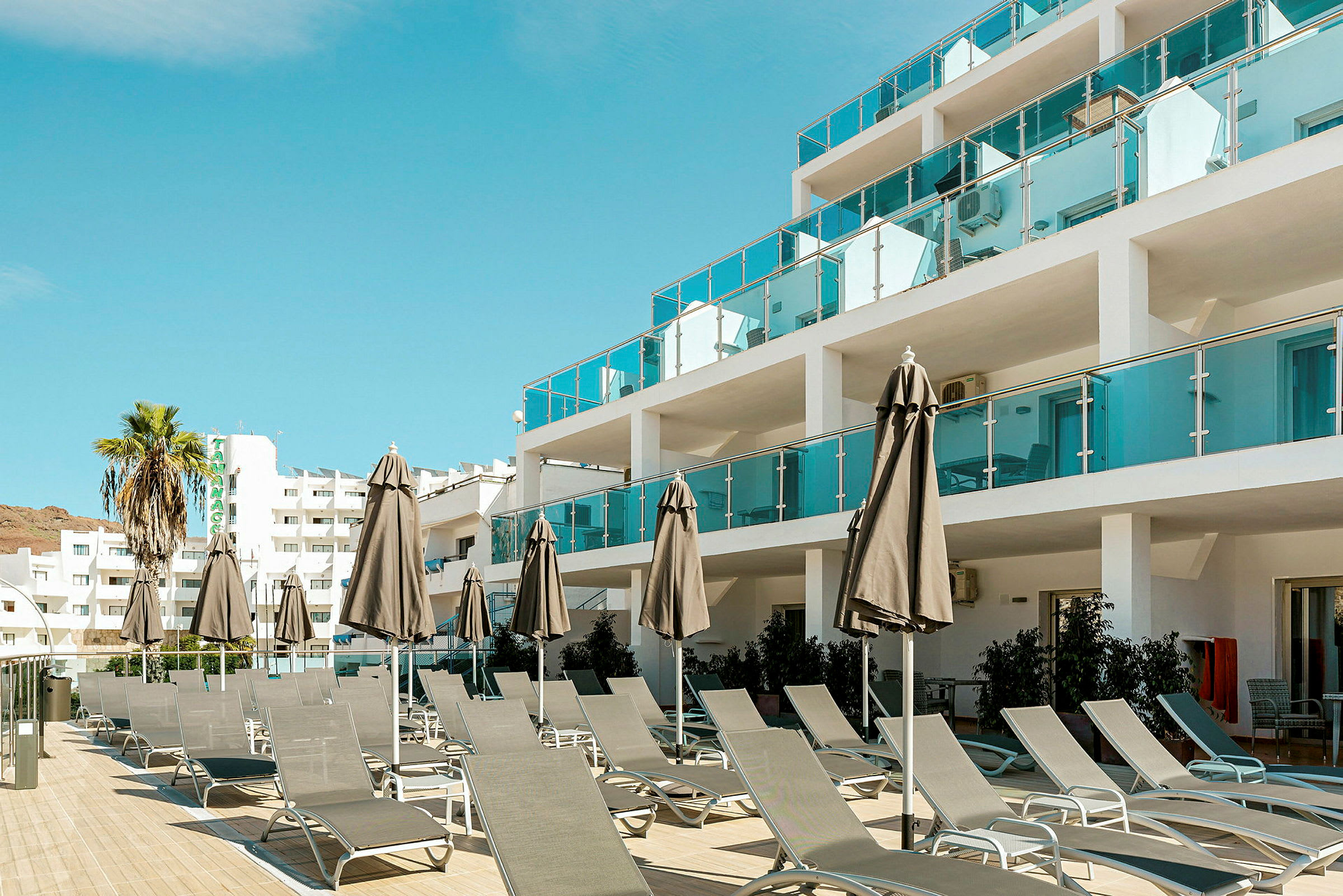 Bilde av en hotellbygning med solsenger og parasoller ved en uteplass. (AI-generert tekst)