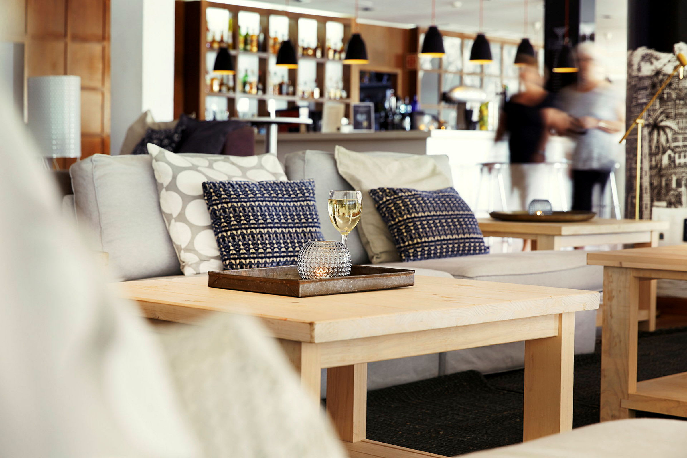 Et sofabord med et glass med drikke foran en sofa i en lounge. (AI-generert tekst)