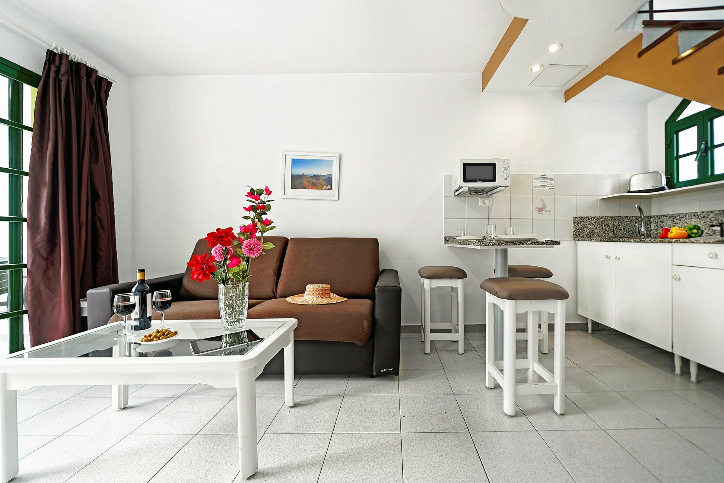 En stue med en sofa, kaffebord med blomster og et kjøkken i bakgrunnen. (AI-generert tekst)