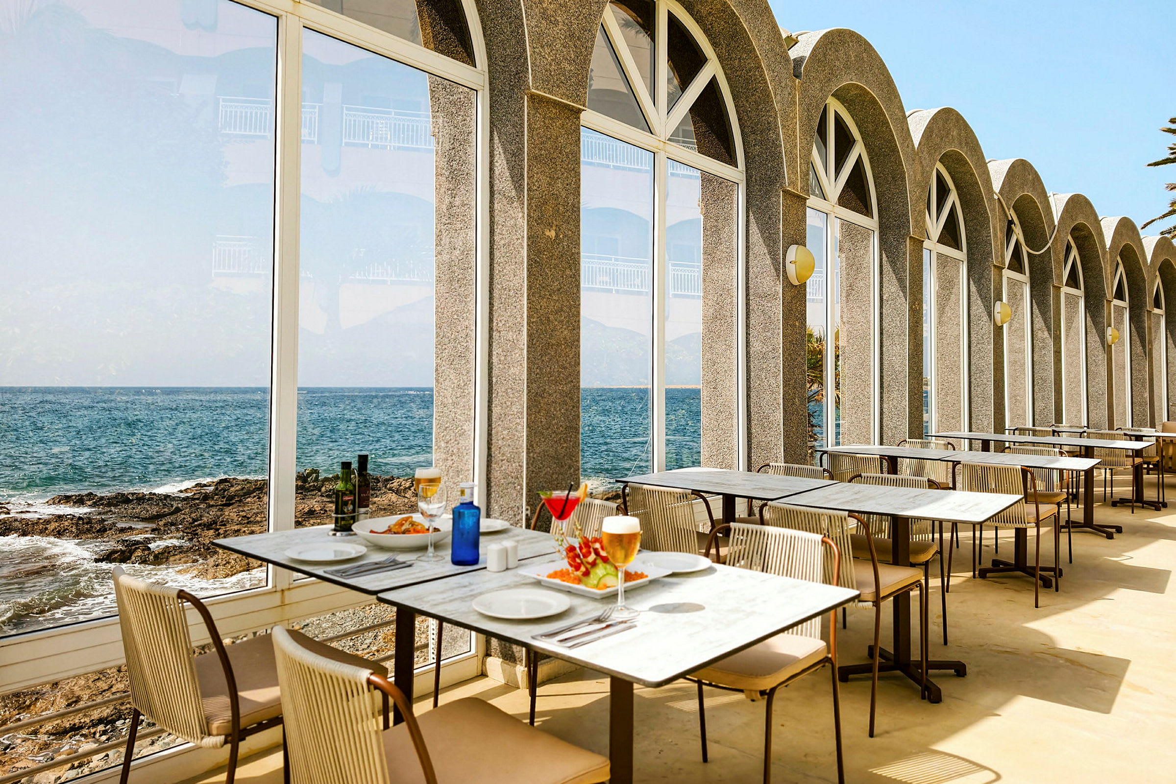 Restauranter med bord plassert ved store glassvinduer som vender mot havet. (AI-generert tekst)