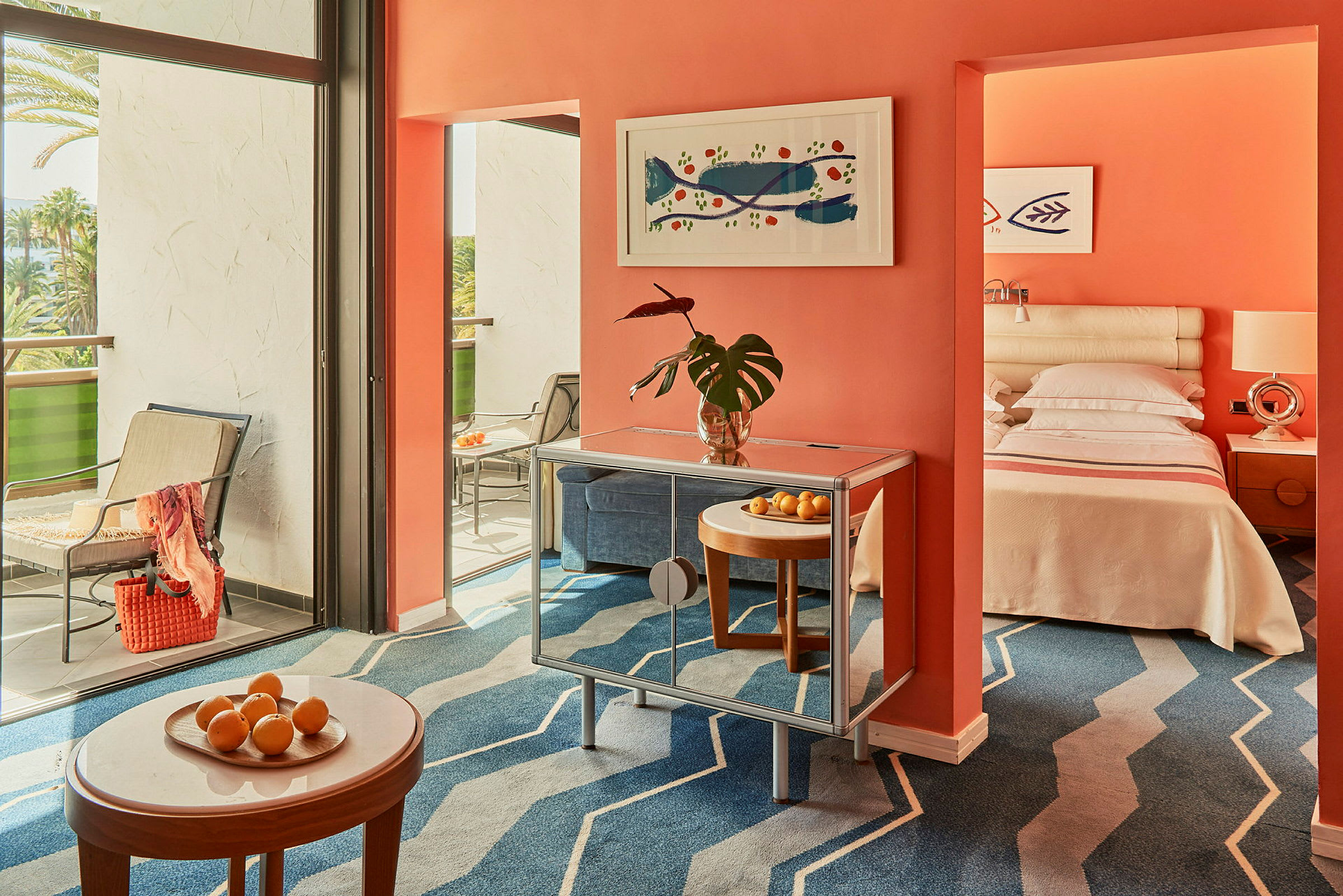 Et hotellrom med en oransje vegg, moderne innredning, balkong og en oppredd seng. (AI-generert tekst)