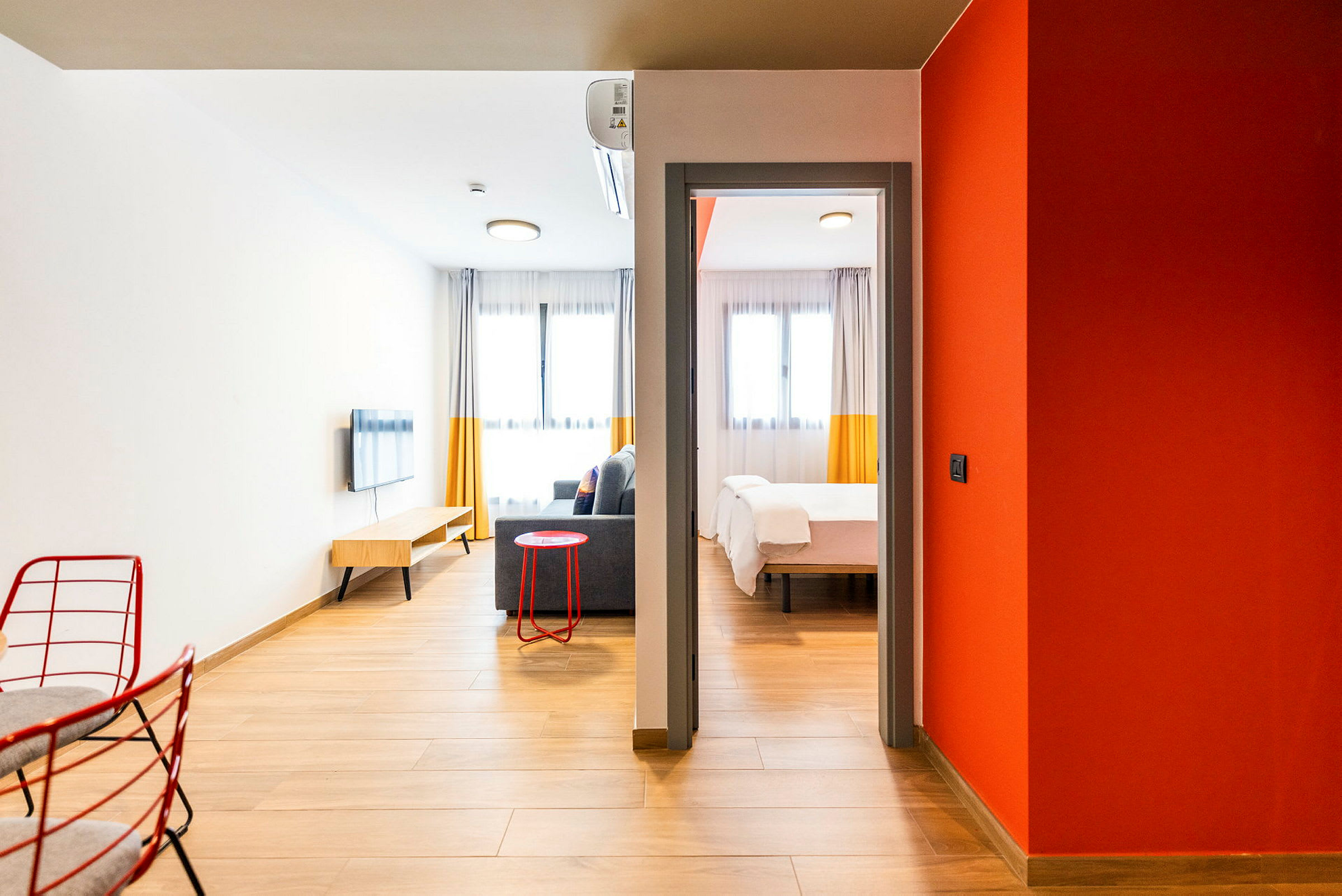Et moderne hotellrom med tregulv og innbydende interiør. Rommet har en sittegruppe med sofa, veggmontert TV og et soverom med en dobbeltseng. (AI-generert tekst)