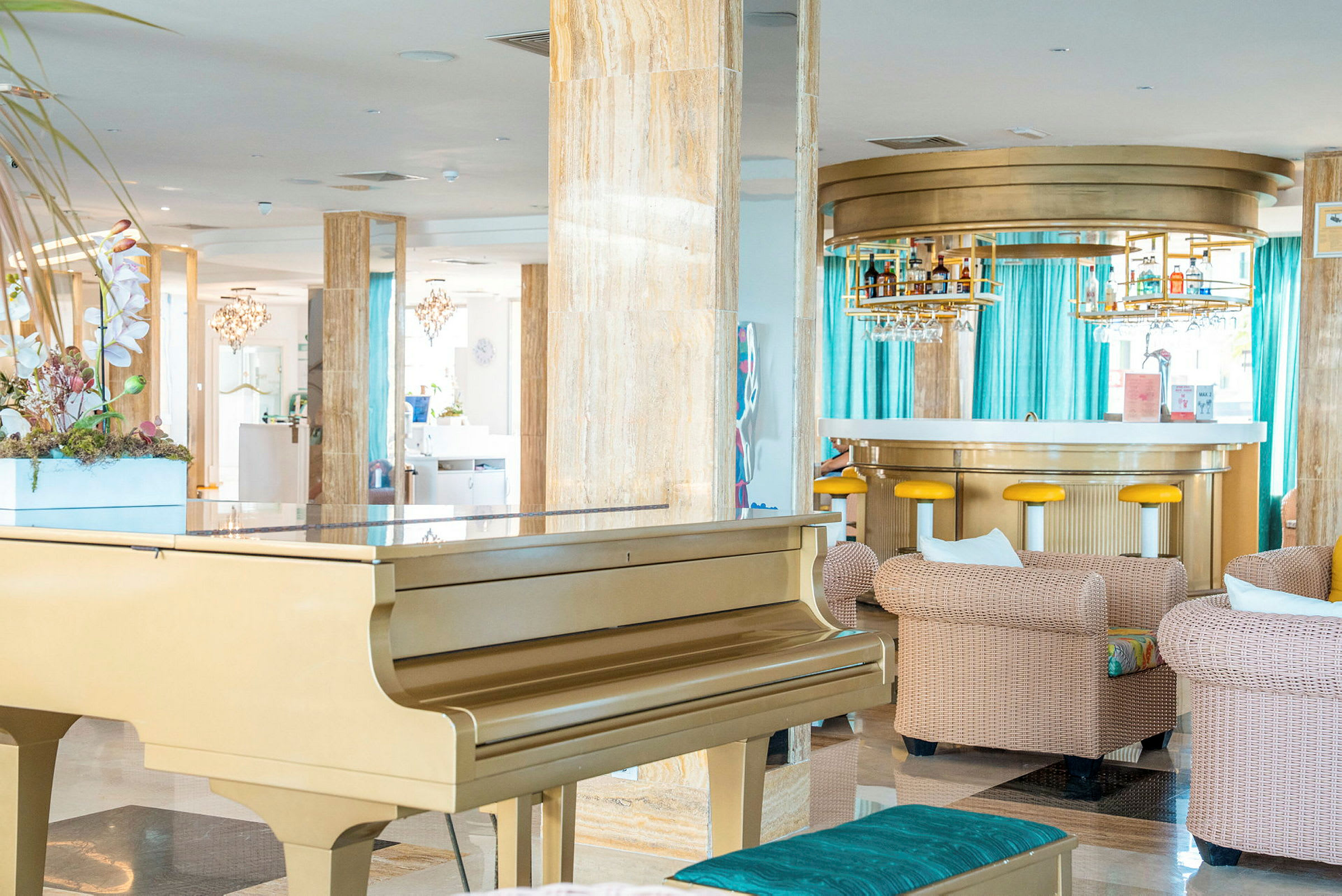Et elegant hotellområde med et gullfarget piano, komfortable sittegrupper og en moderne bar i bakgrunnen. (AI-generert tekst)