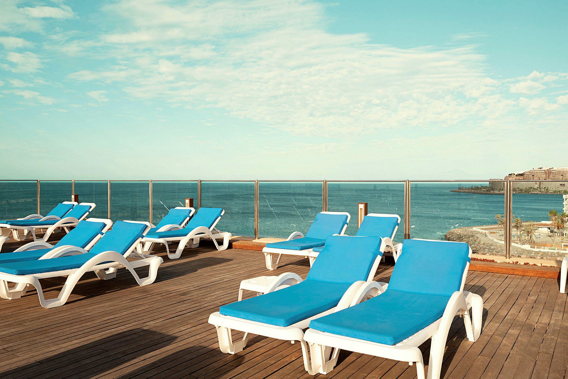Solsenger med blå puter på en terrasse, med utsikt over havet. (AI-generert tekst)
